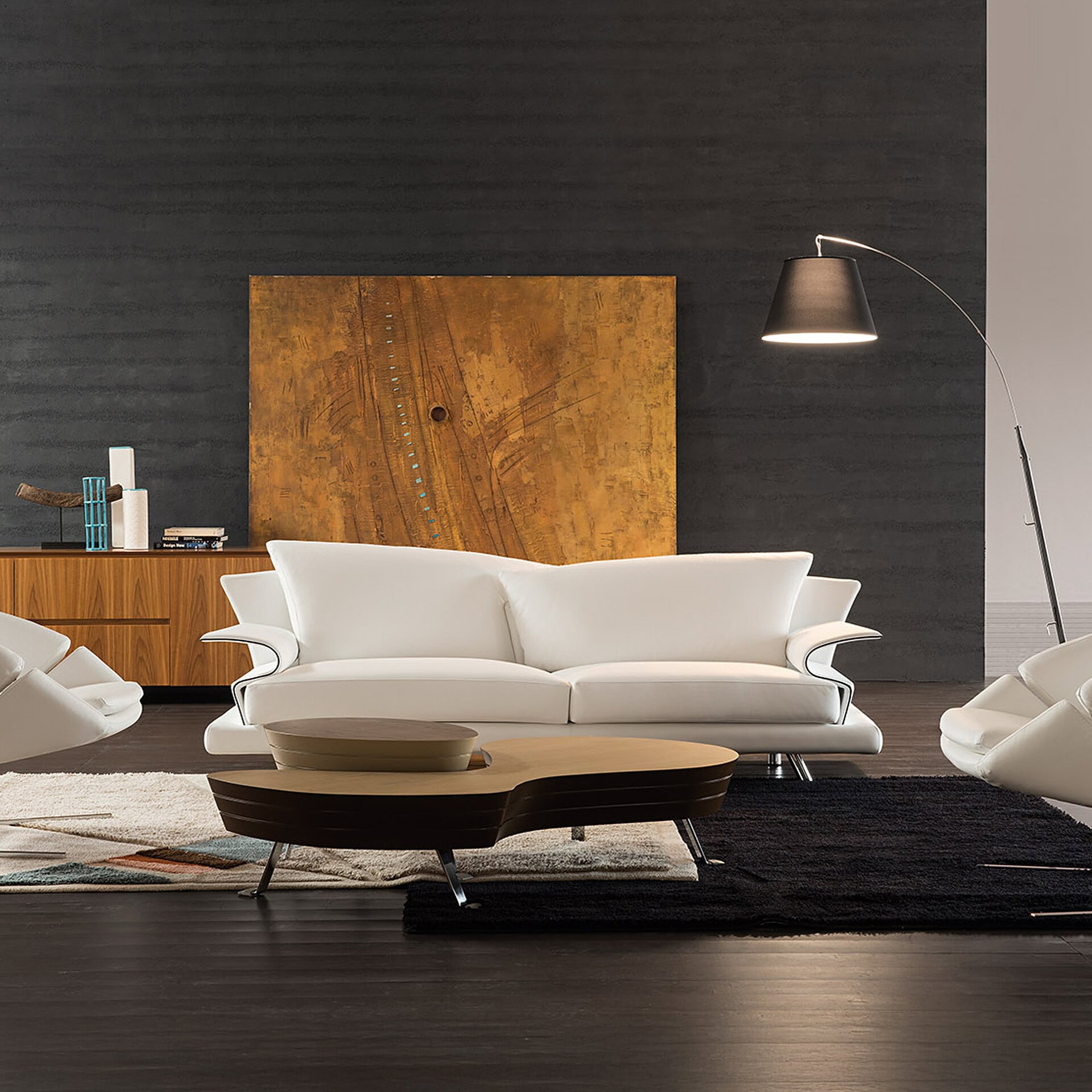 A modern living room with a white leather sofa, a unique two-tiered coffee table, and dark textured walls featuring a large abstract artwork and a wooden credenza. An arc floor lamp illuminates the scene.