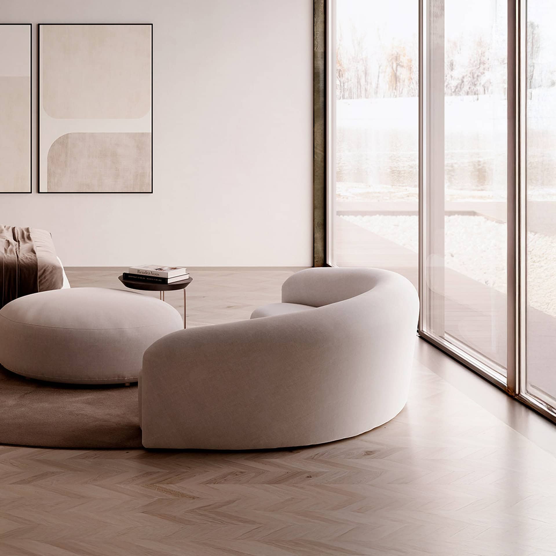 A modern living room with a curved beige sofa, a round ottoman, and minimalist abstract art on a white wall. Large windows overlook a bright, snowy winter scene.