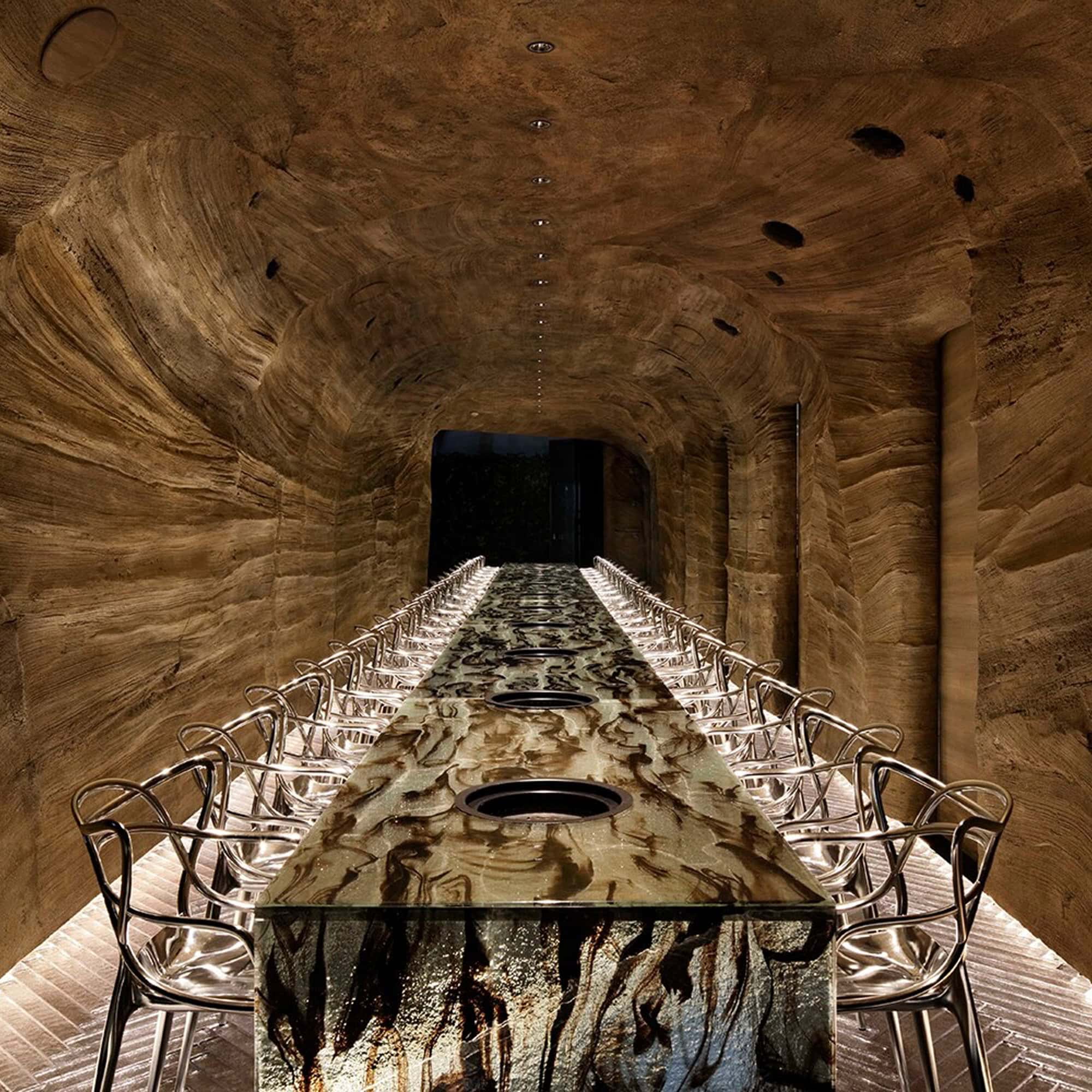 Long rustic dining table surrounded by Masters Metal Dining Chairs in a dramatic tunnel-like interior.