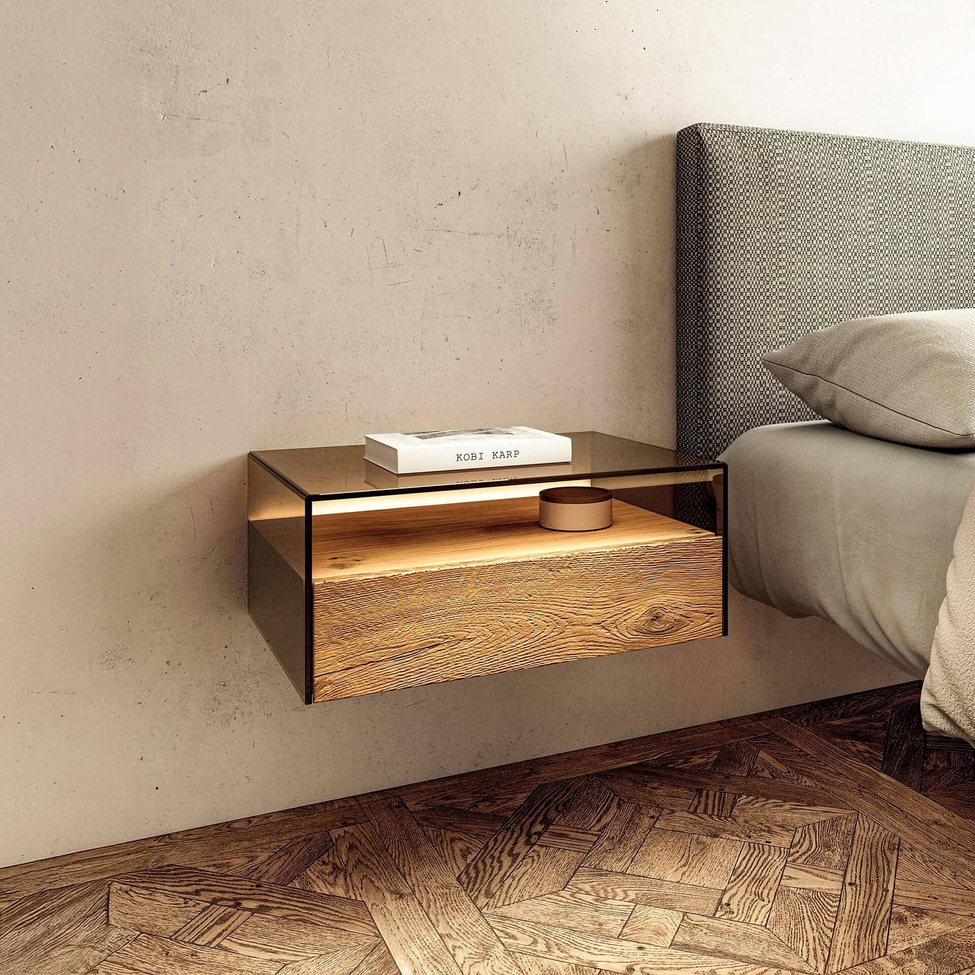 Hom Bedside Table styled beside a modern bed with smoked glass top and wooden drawer.
