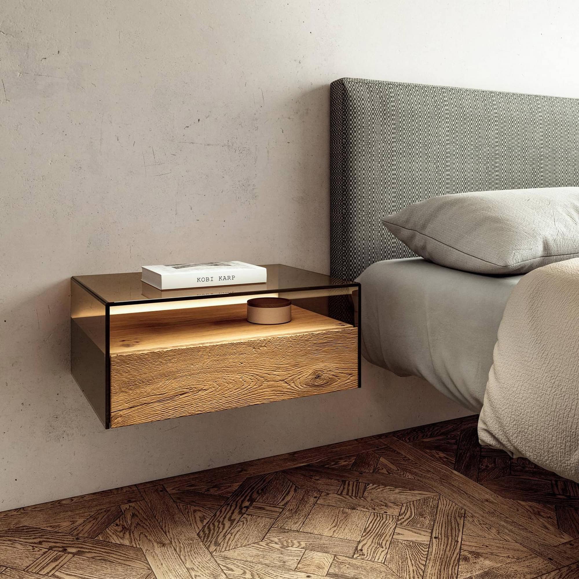 Hom Bedside Table styled beside a modern bed with smoked glass top and wooden drawer.