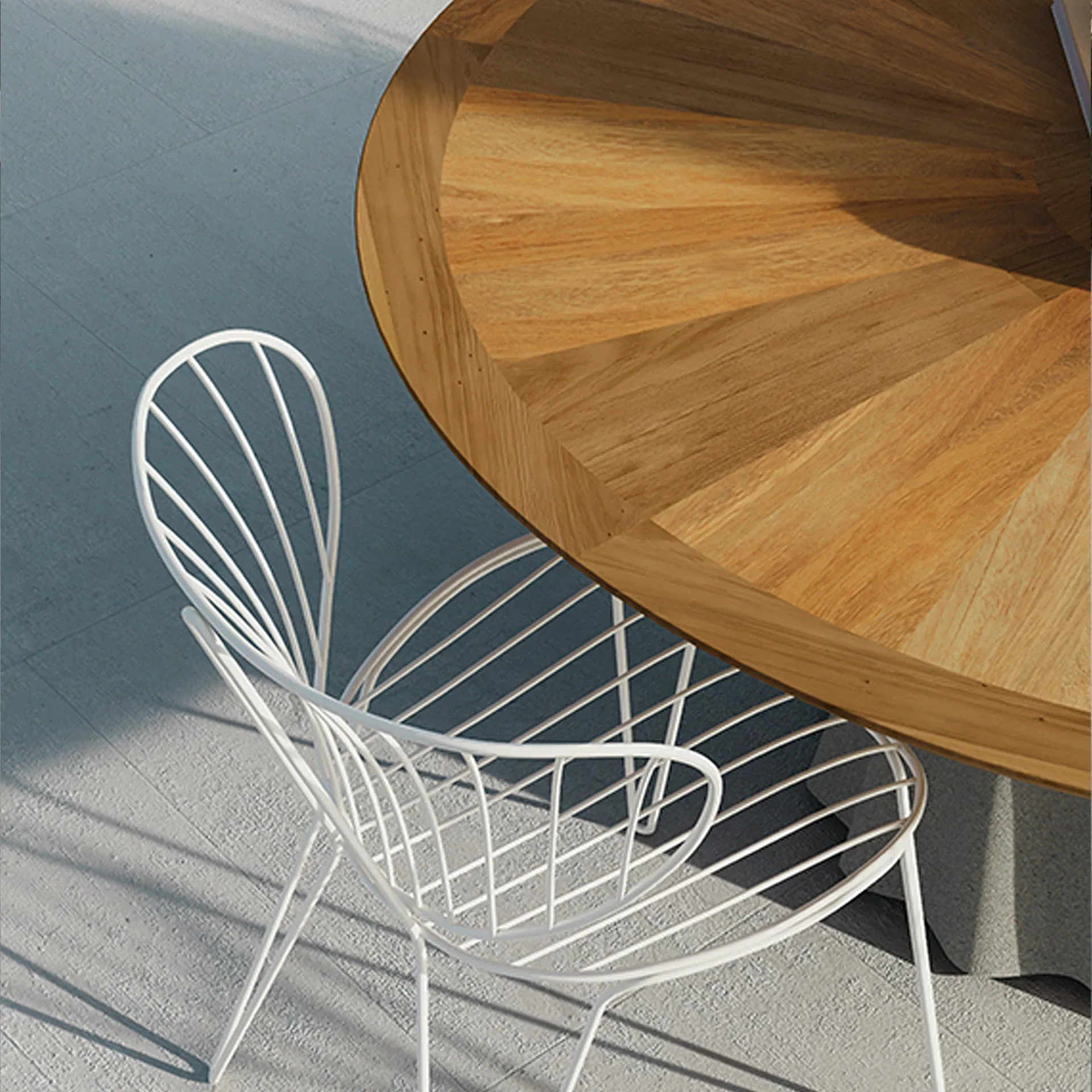Overhead view of a white wire chair and a round wooden table on a light gray tiled floor, casting long shadows.