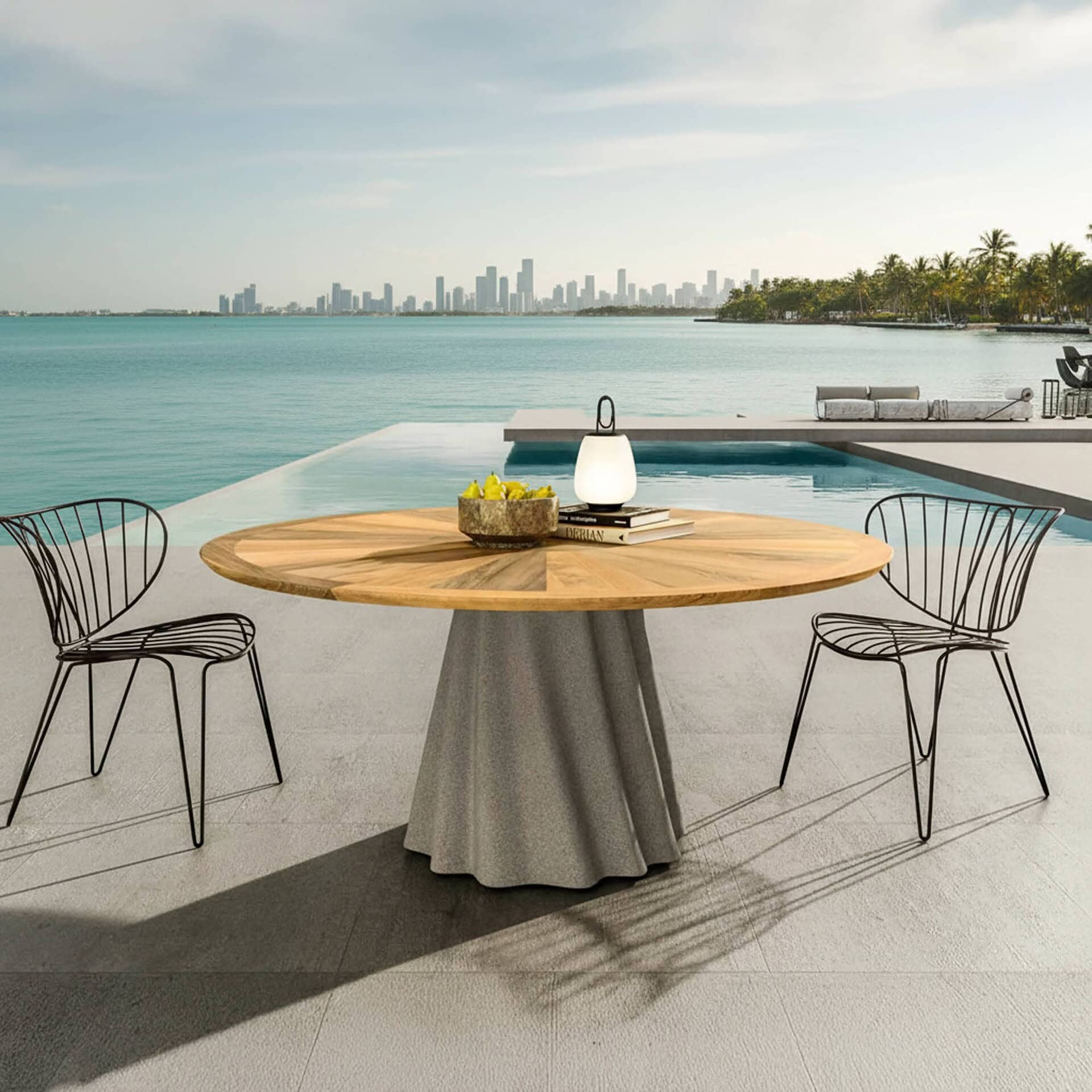 Onda Round Outdoor Dining Table with Iroko wood top and concrete base, positioned by an ocean view pool.