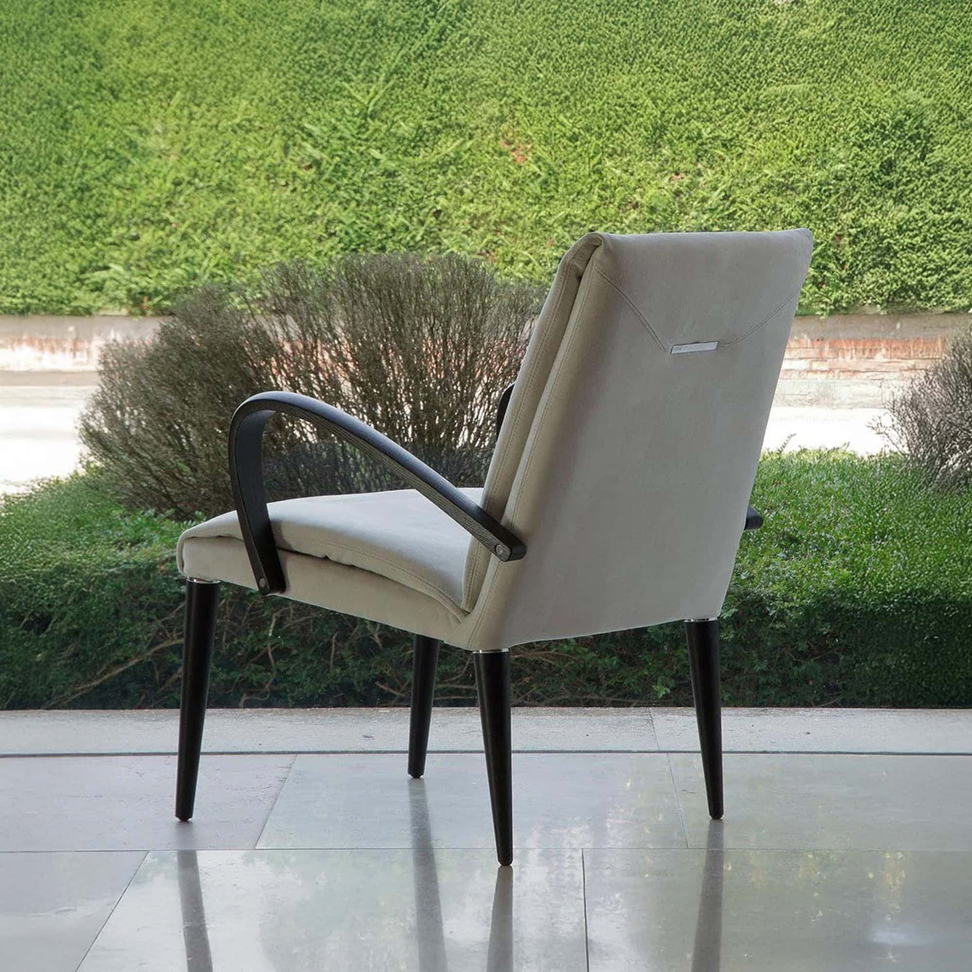 Soft Armchair with light upholstered seat and dark curved arms, shown outdoors with greenery in the background