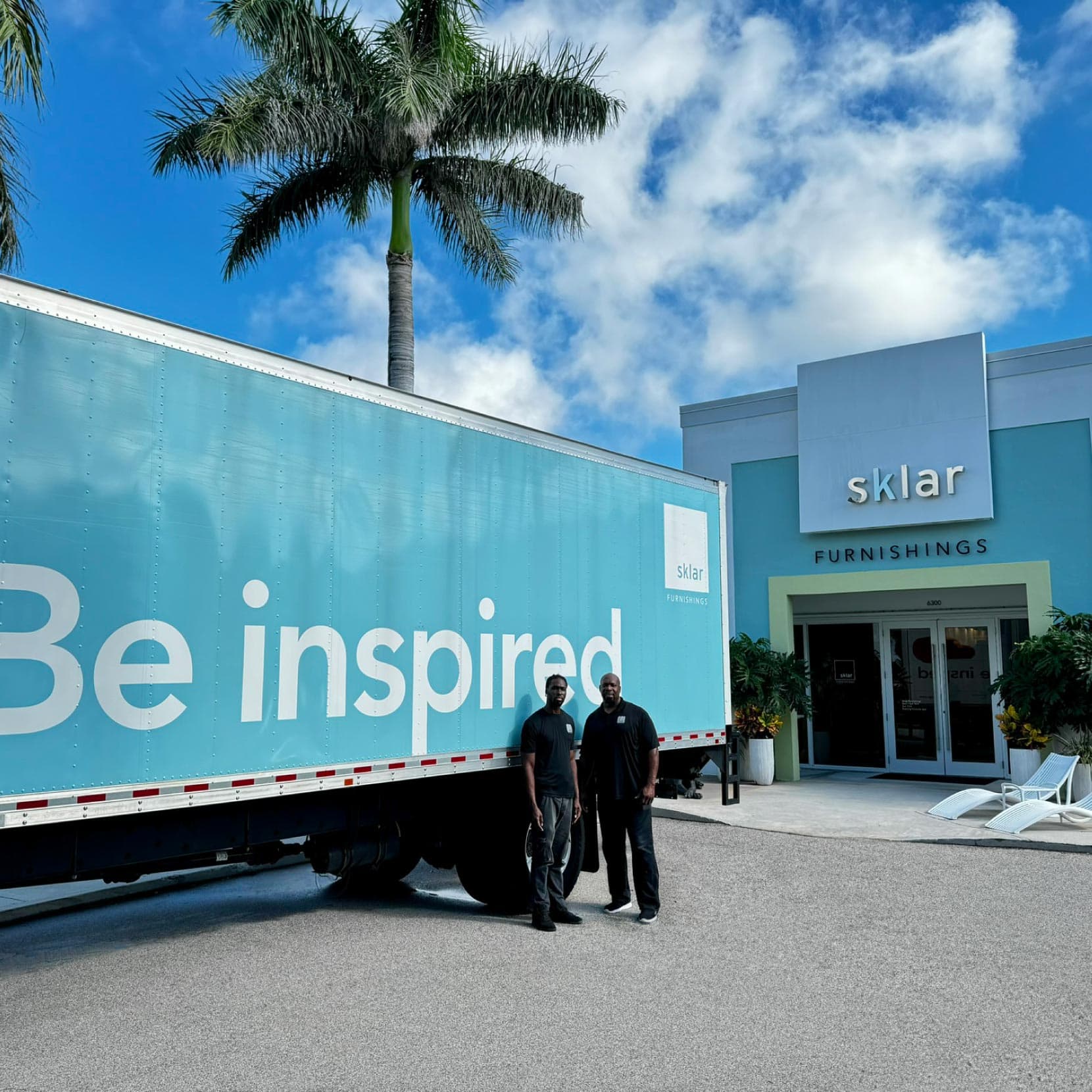 Modern furniture store exterior featuring delivery truck and tropical landscaping.