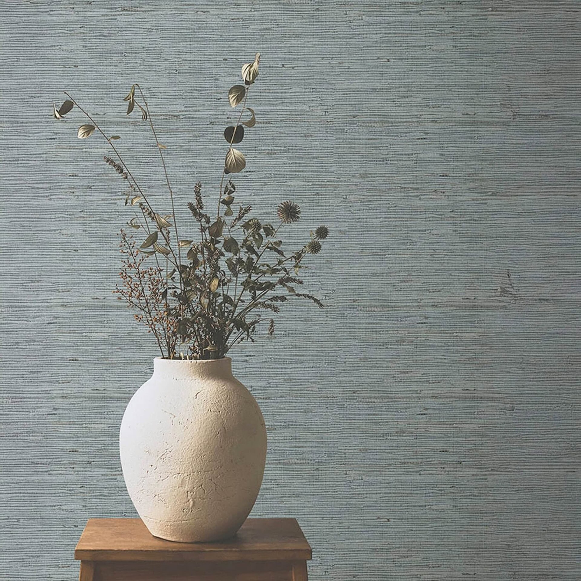 Rustic white textured ceramic vase with dried botanical arrangement on wooden table, minimalist decor.