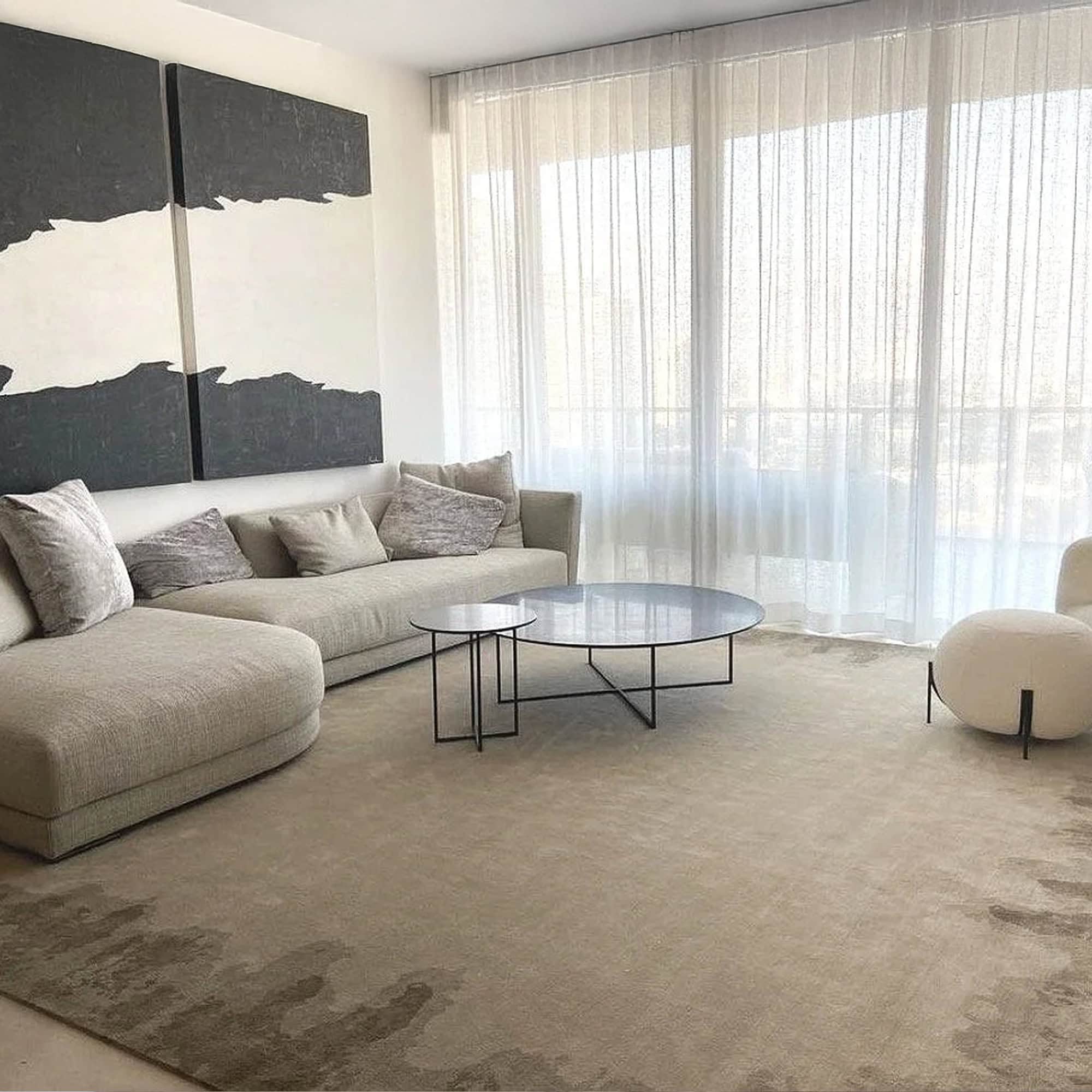 Contemporary living room with neutral-toned sofa, round coffee tables, and large windows with sheer curtains.
