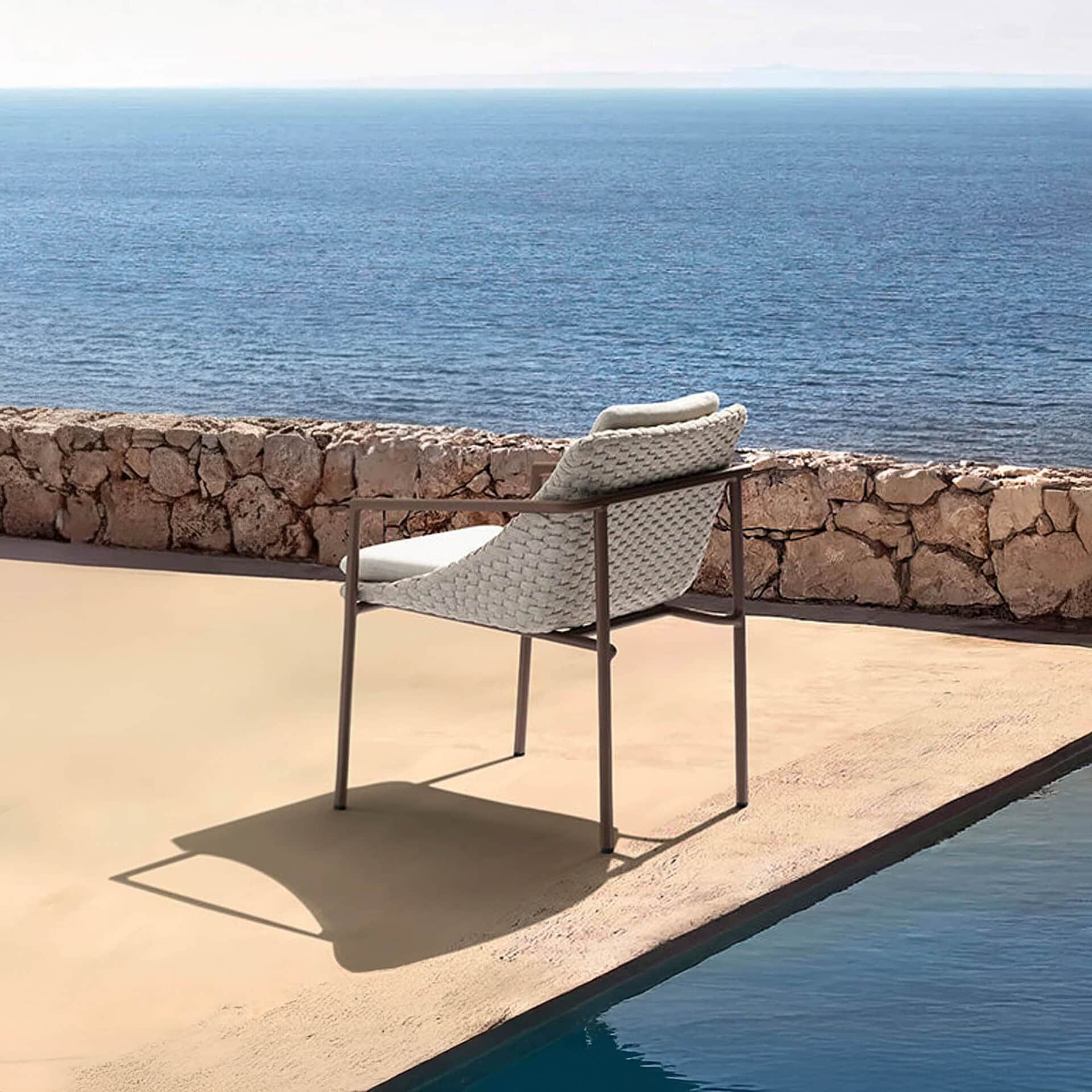 Modern outdoor chair with woven texture and cushions, overlooking the ocean on a sunny terrace.