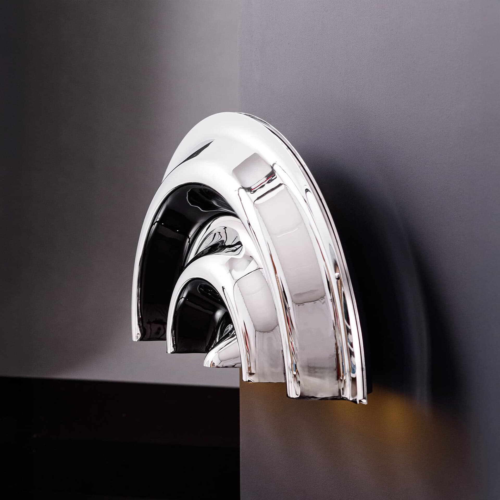 Shiny metallic rainbow sculpture on dark wall, modern art decor piece.