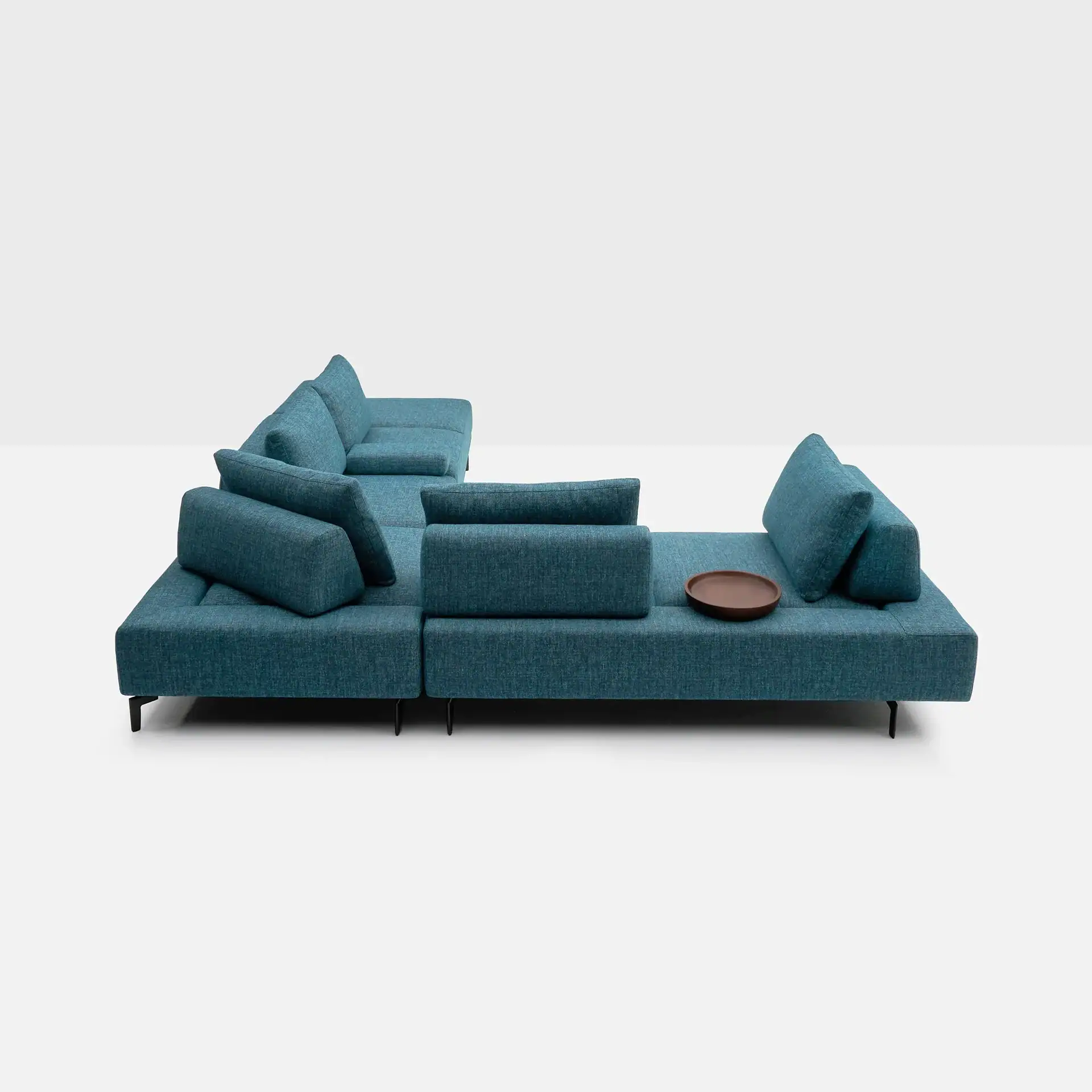 A teal modular L-shaped sofa with black legs and a small brown tray on a light gray background.
