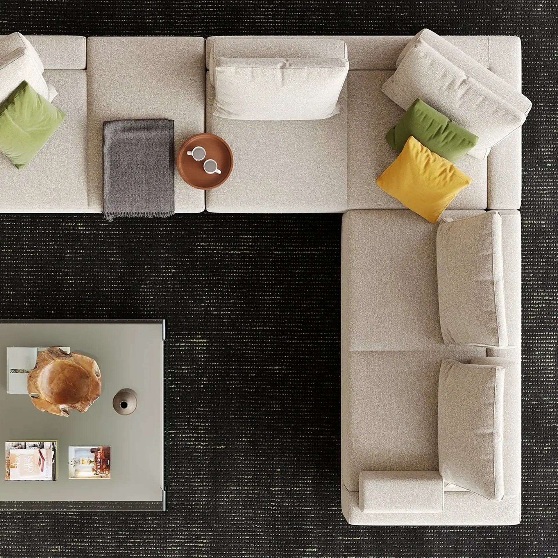 Overhead view of a light beige L-shaped sectional sofa with green and yellow pillows, a gray blanket, and a wooden tray with mugs. A gray coffee table with a wooden bowl and books is in the foreground, all on a dark textured rug.