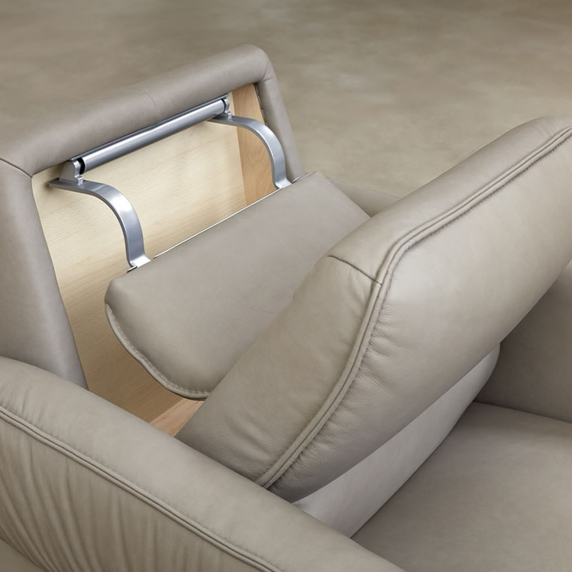 Close-up of a modern light beige leather armchair with an adjustable headrest mechanism made of brushed metal and light wood.