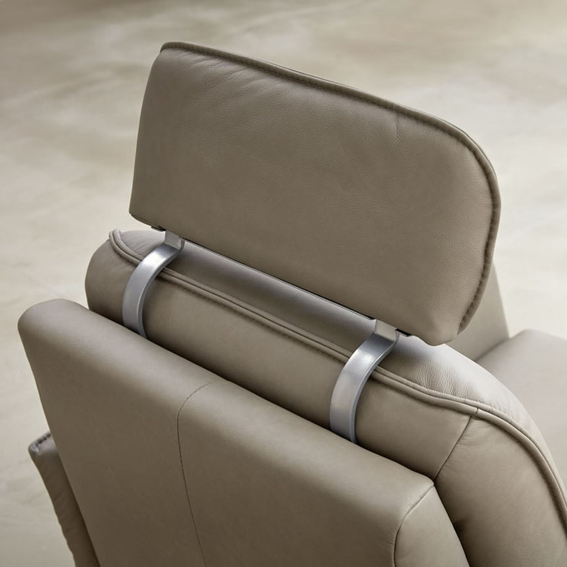 Close-up of a taupe leather chair's headrest, connected by curved silver metal supports to the backrest.