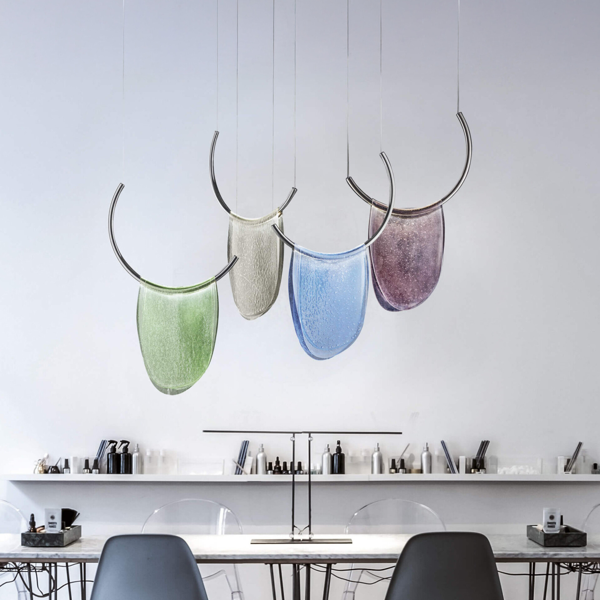 Colorful modern glass pendant lights with curved chrome accents hanging above a minimalist dining table.