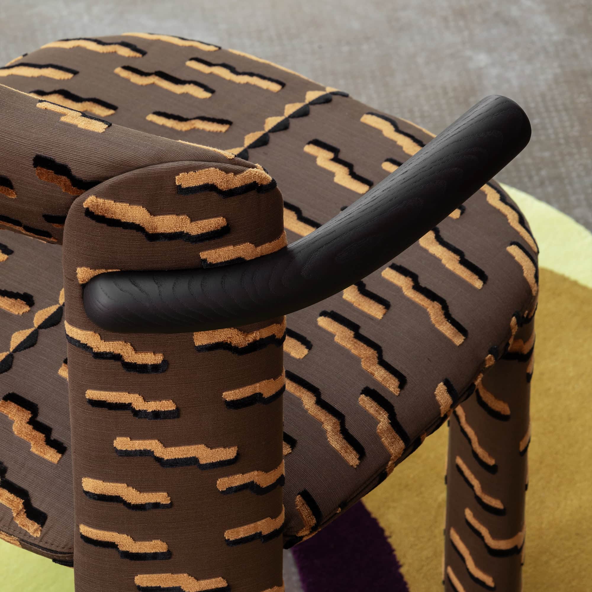 Luxurious patterned armchair with modern design, bold fabric, and sleek black wooden armrest.