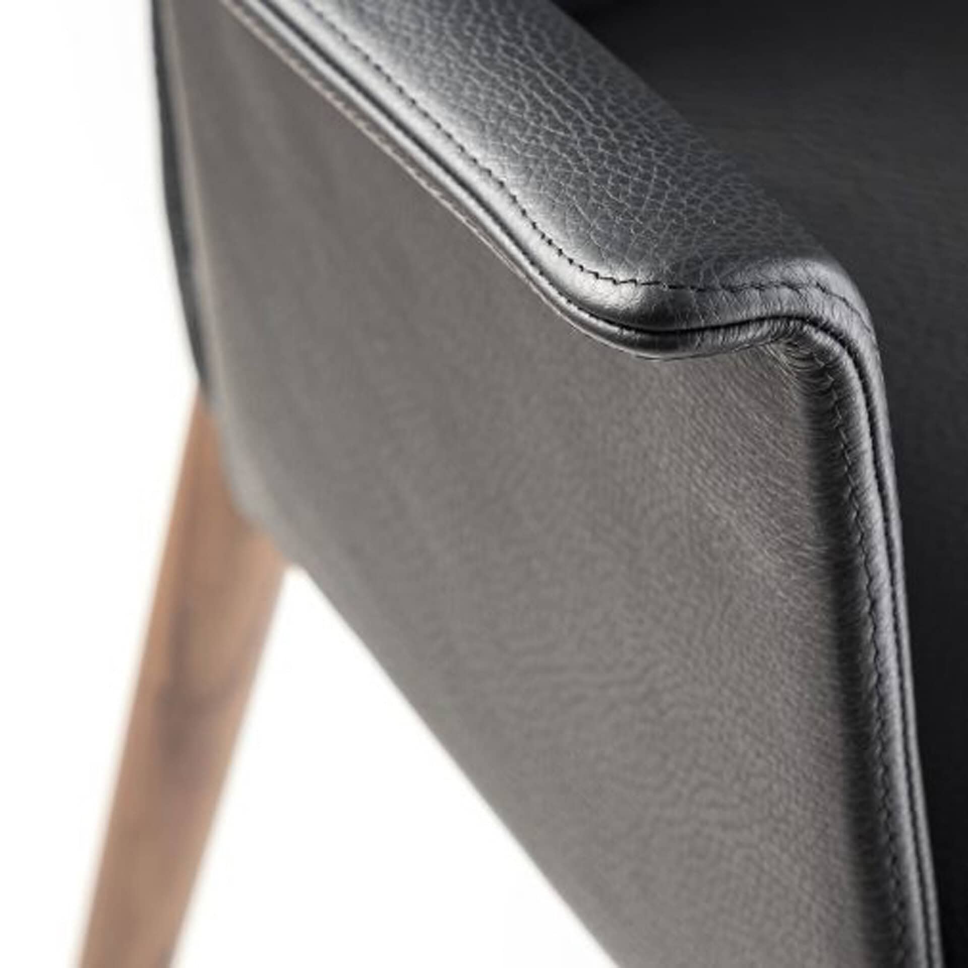 Close-up of black leather upholstered chair with wooden legs.