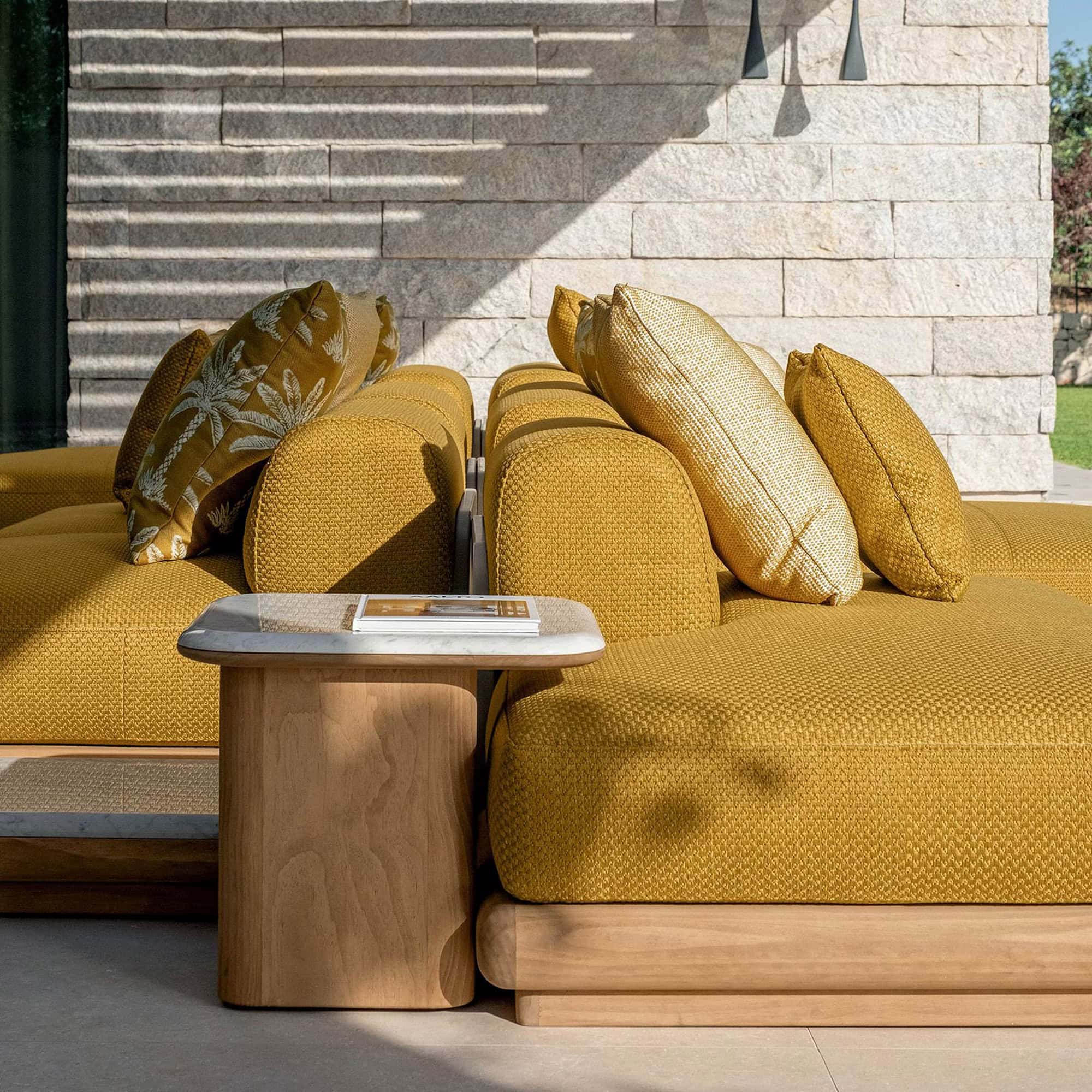 Yellow modern outdoor sectional sofa with decorative pillows, stylish wooden side table, and stone wall backdrop.
