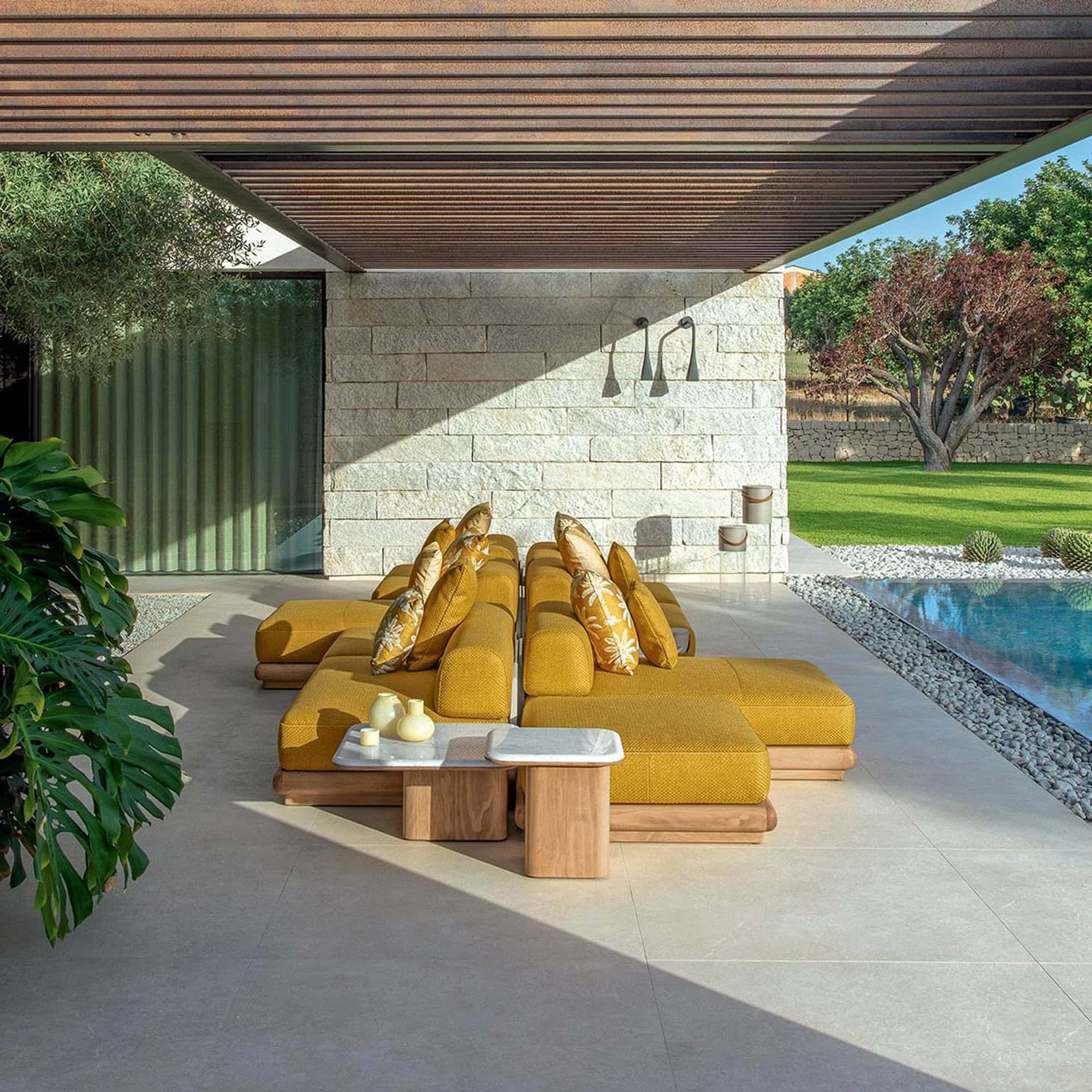 Modern outdoor lounge with yellow cushioned sectional and side tables by a pool, under a covered patio.