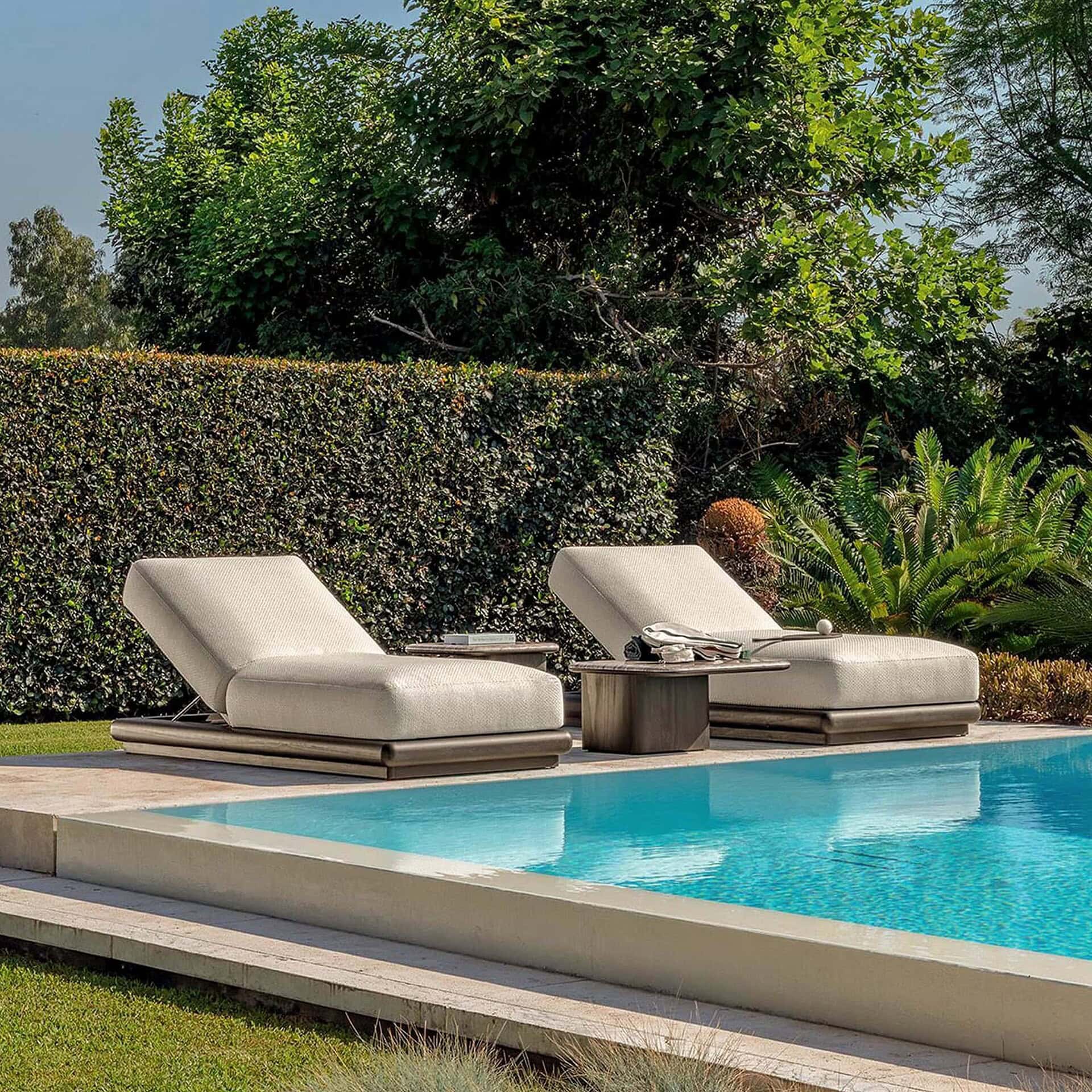 Luxurious outdoor chaise lounges with plush cushions near a modern swimming pool and lush greenery.