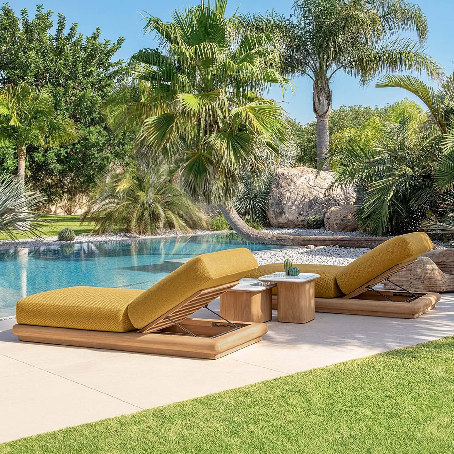 Luxurious outdoor teak chaise lounges with yellow cushions by a poolside surrounded by lush tropical greenery.