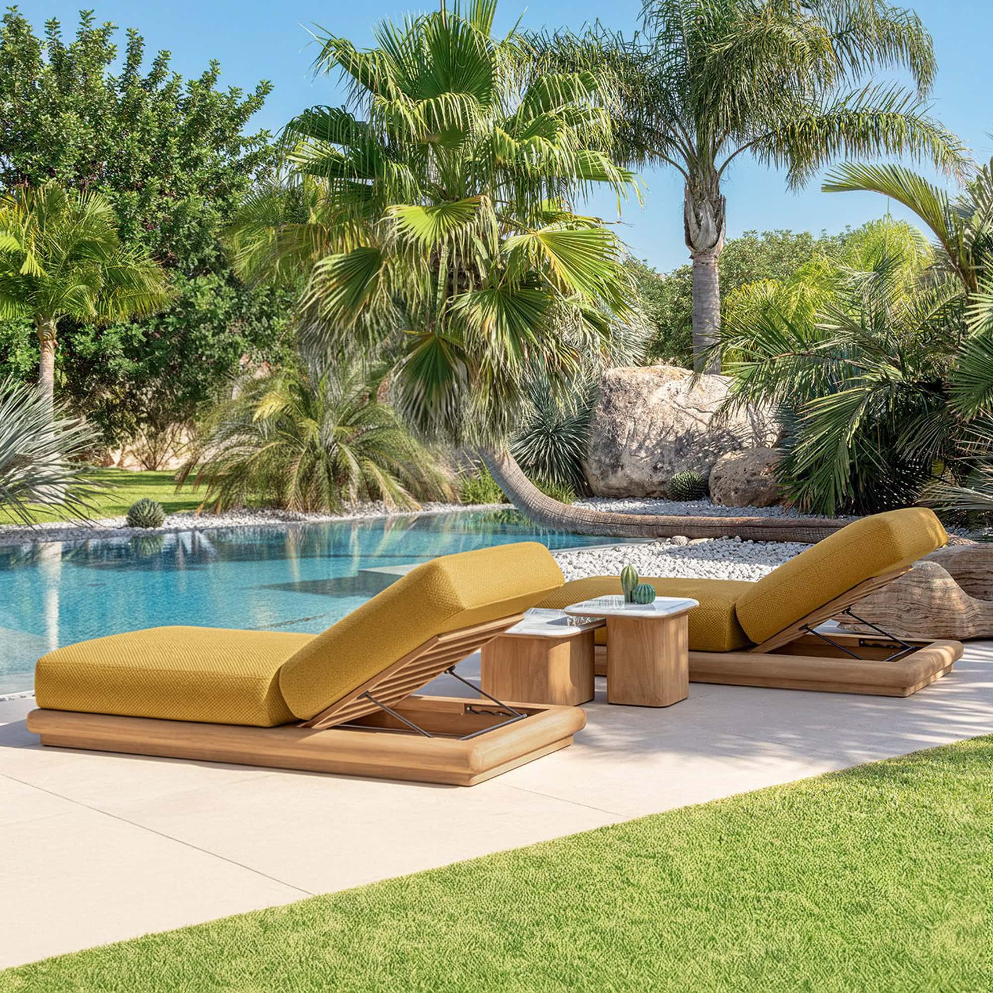 Luxurious outdoor teak chaise lounges with yellow cushions by a poolside surrounded by lush tropical greenery.