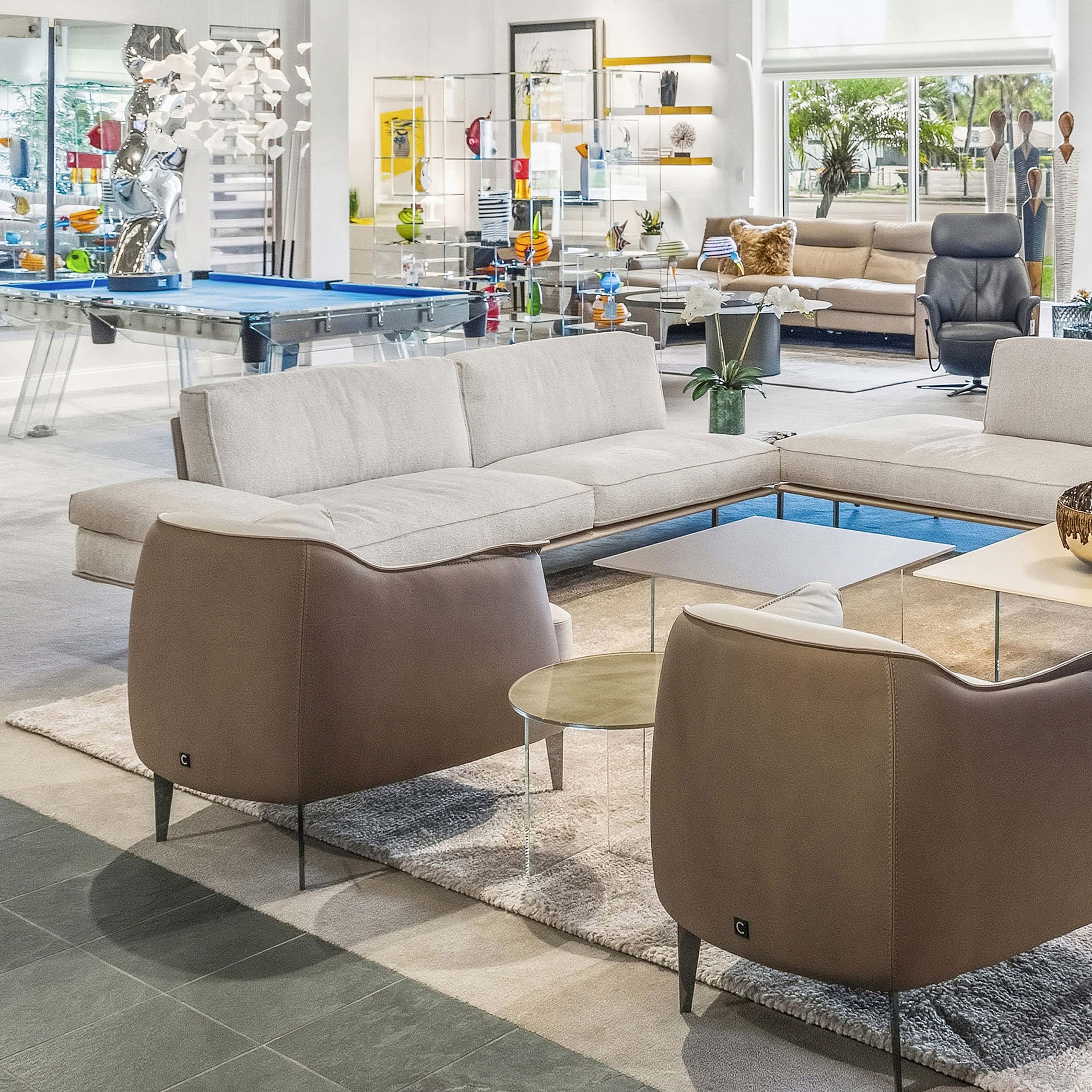 Contemporary living room with modern beige sofas, accent chairs, and sleek glass tables in a stylish showroom setting.