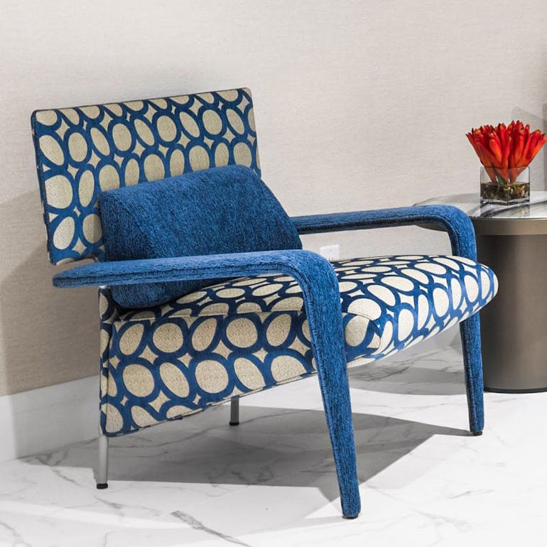 Blue patterned armchair with velvet cushion and modern side table with flower arrangement, stylish furniture from Sklar Furnishings.