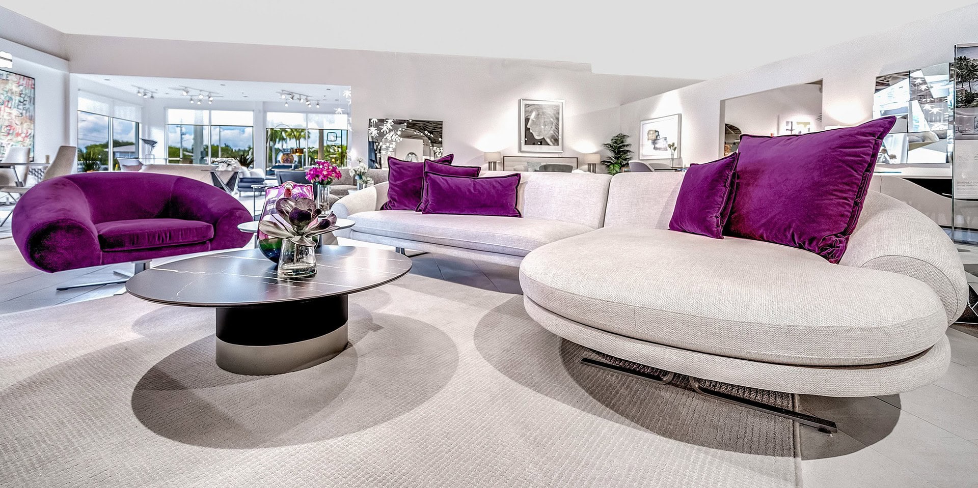 Soft contemporary sectional sofa with purple accent pillows in modern living room with glass windows and bright decor.