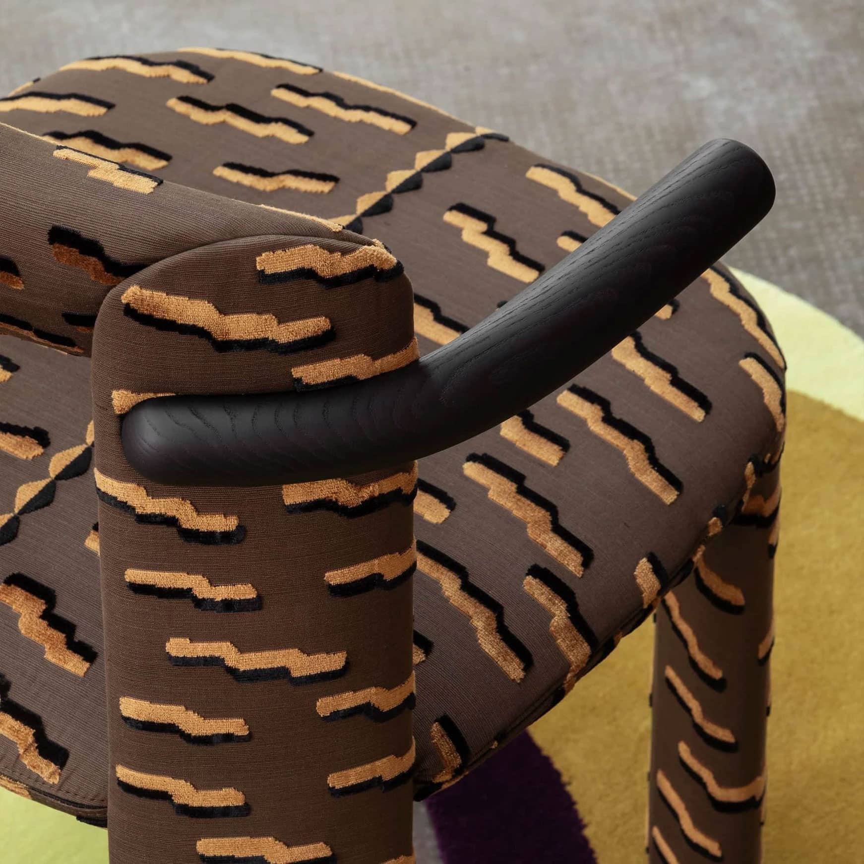 Stylish patterned armchair with black wooden armrest, modern design, and textured upholstery.