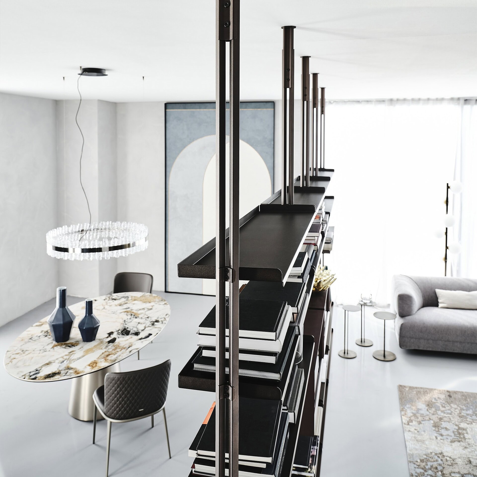 Modern black shelving unit in contemporary living room with dining area and gray sofa.