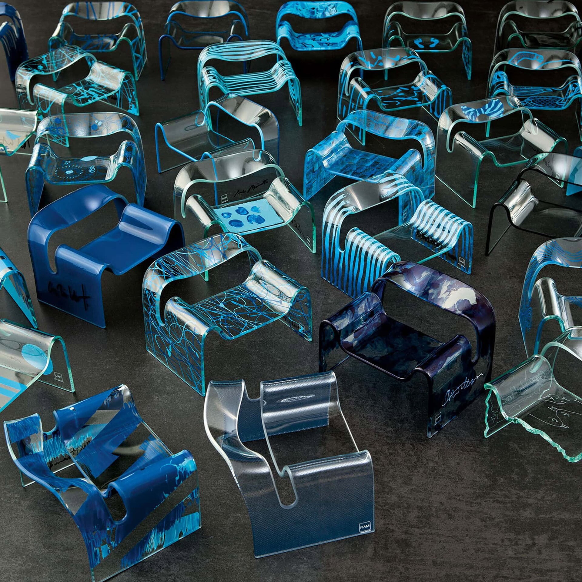 Colorful modern acrylic chairs in blue, black, and clear designs on dark flooring at Sklar Furnishings.
