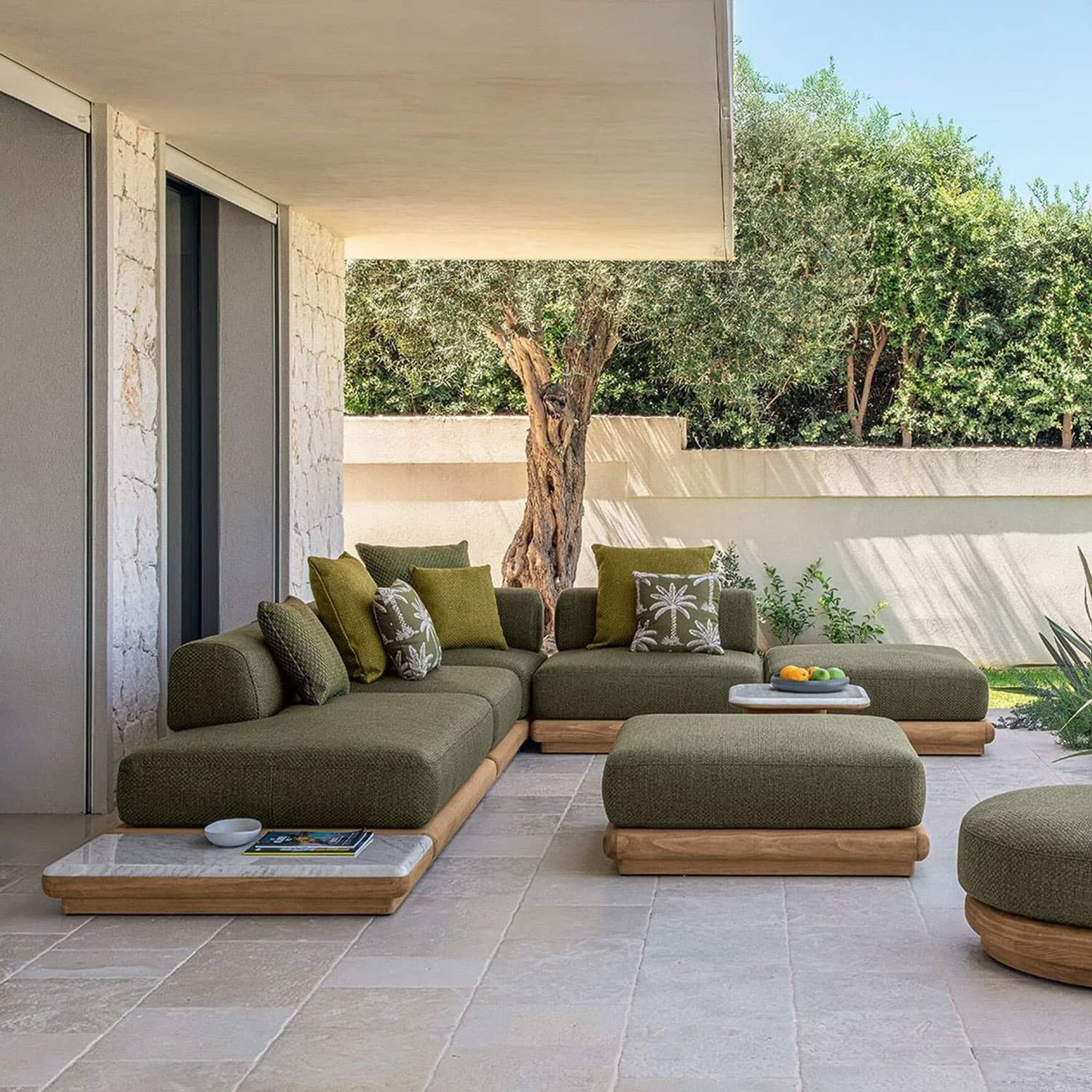 Luxurious outdoor sectional sofa with green cushions and wooden accents under a shaded patio.