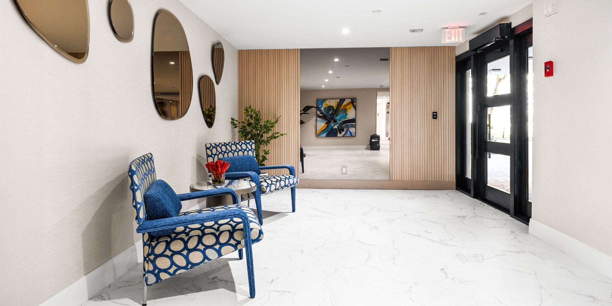 Modern hotel lobby with stylish seating and contemporary decor, featuring blue patterned chairs and wall mirrors.