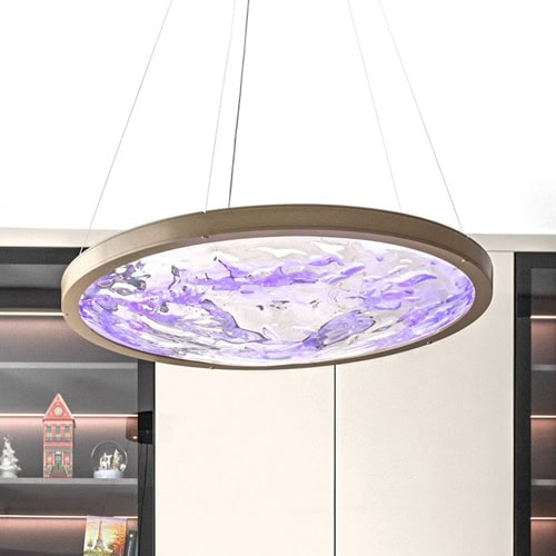 A modern, circular pendant light fixture with a bronze frame and a textured, rippled inner panel glowing with vibrant purple light, suspended in a contemporary room.