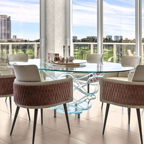 A modern round glass coffee table with a clear top and a sculptural base made of wavy, layered clear glass panels, against a white background.