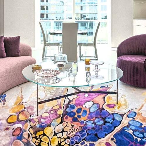 Bright condo living room featuring a vibrant, abstract-patterned rug and a sleek glass coffee table.