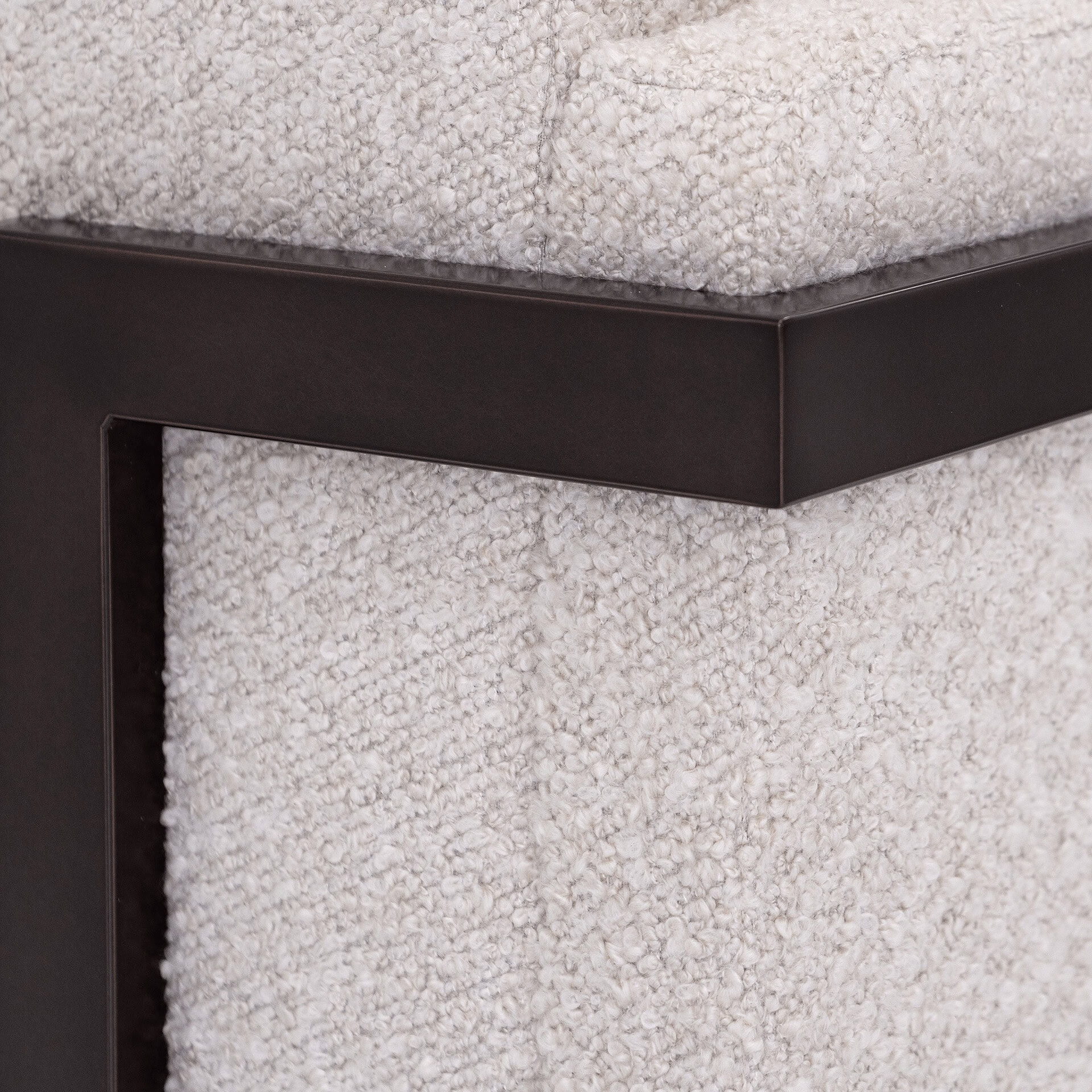 Close-up of light, textured boucle fabric against a dark, angular metal frame, highlighting material contrast.