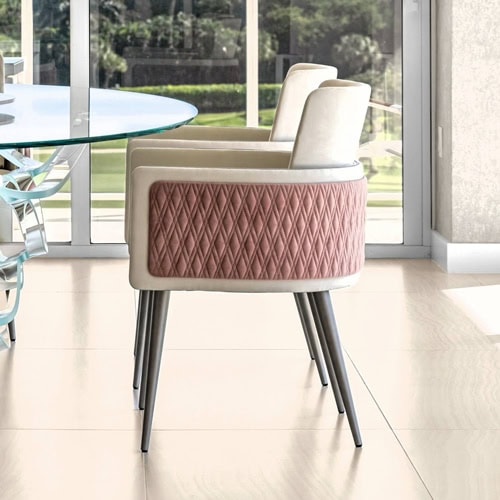 Two modern dining chairs with cream upholstery and dusty rose quilted backs, featuring tapered dark legs, beside a glass table in a bright room with large windows overlooking greenery.