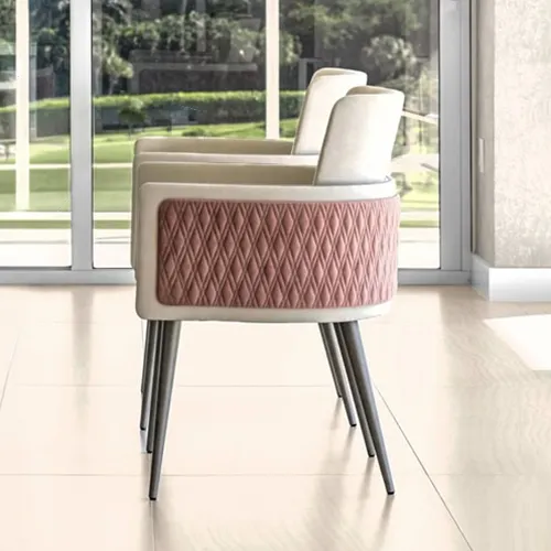 Two modern dining chairs with cream upholstery and dusty rose quilted backs, featuring tapered dark legs, beside a glass table in a bright room with large windows overlooking greenery.