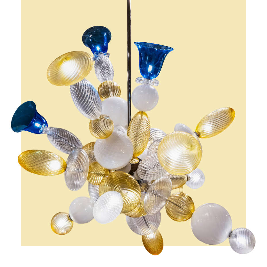 A luxurious contemporary chandelier made of clustered hand-blown glass elements in gold, silver, white, and blue, against a pale yellow background.
