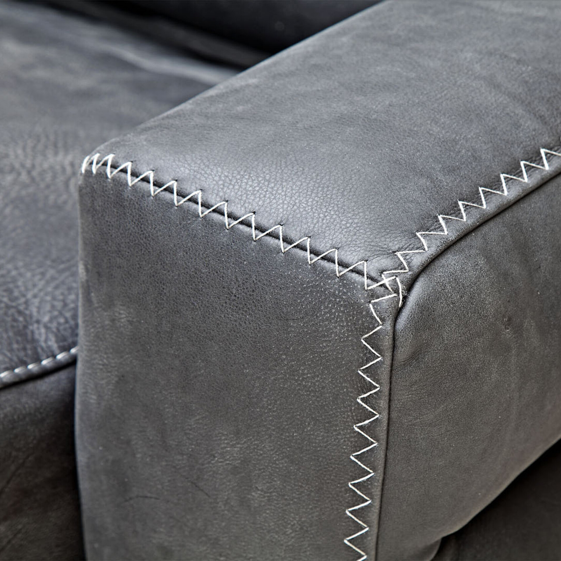 Close-up of dark gray leather furniture with prominent white zigzag stitching along its seams and edges.