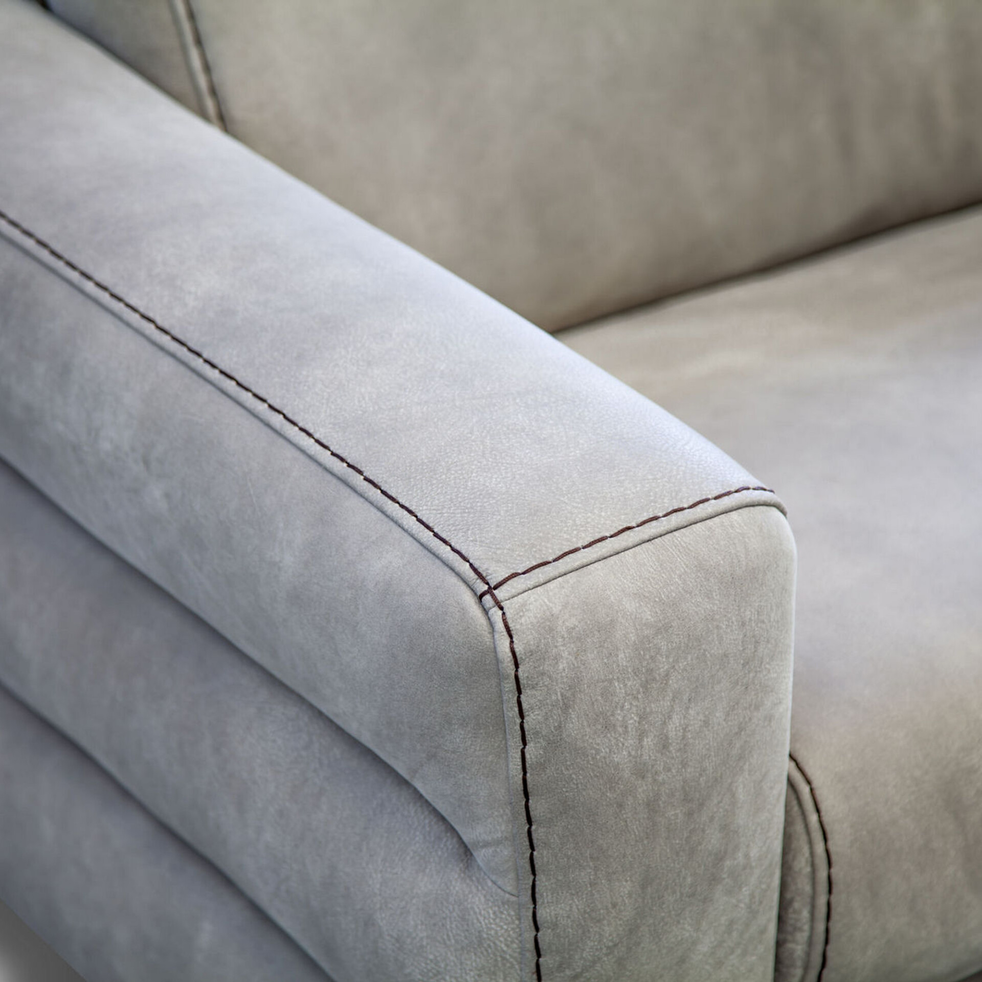 Close-up of a light grey sofa armrest with dark brown contrasting stitching along its edges.