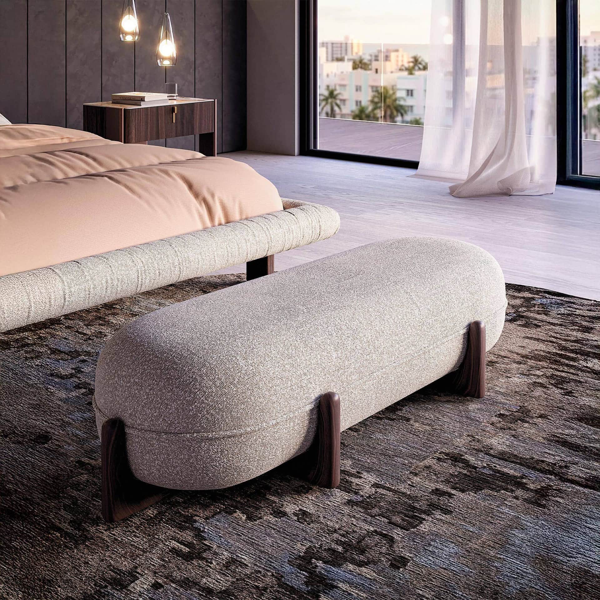 A modern bedroom with a beige upholstered bench in the foreground, a bed with peach bedding, and a large window revealing a city and ocean view. Dark wood furniture and pendant lights complete the luxurious scene.