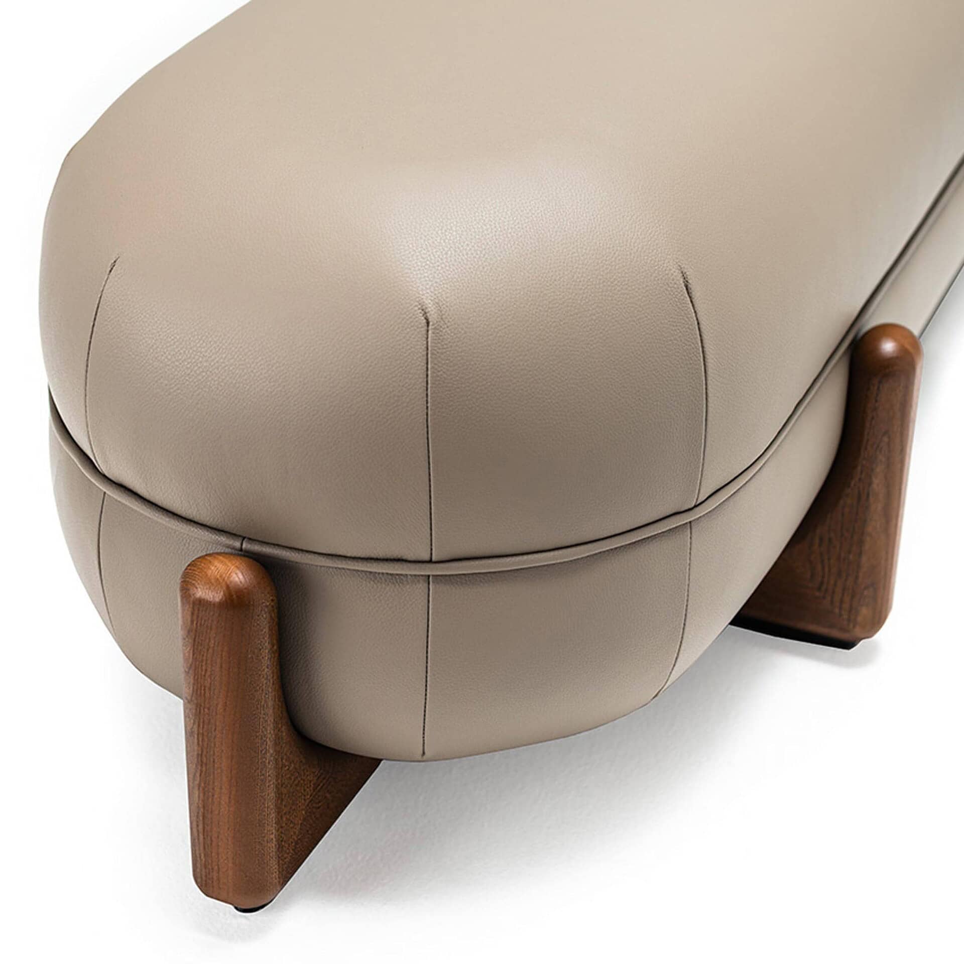 Close-up of a modern beige leather bench with rounded, fluted ends and dark, sculptural wooden legs, against a white background.
