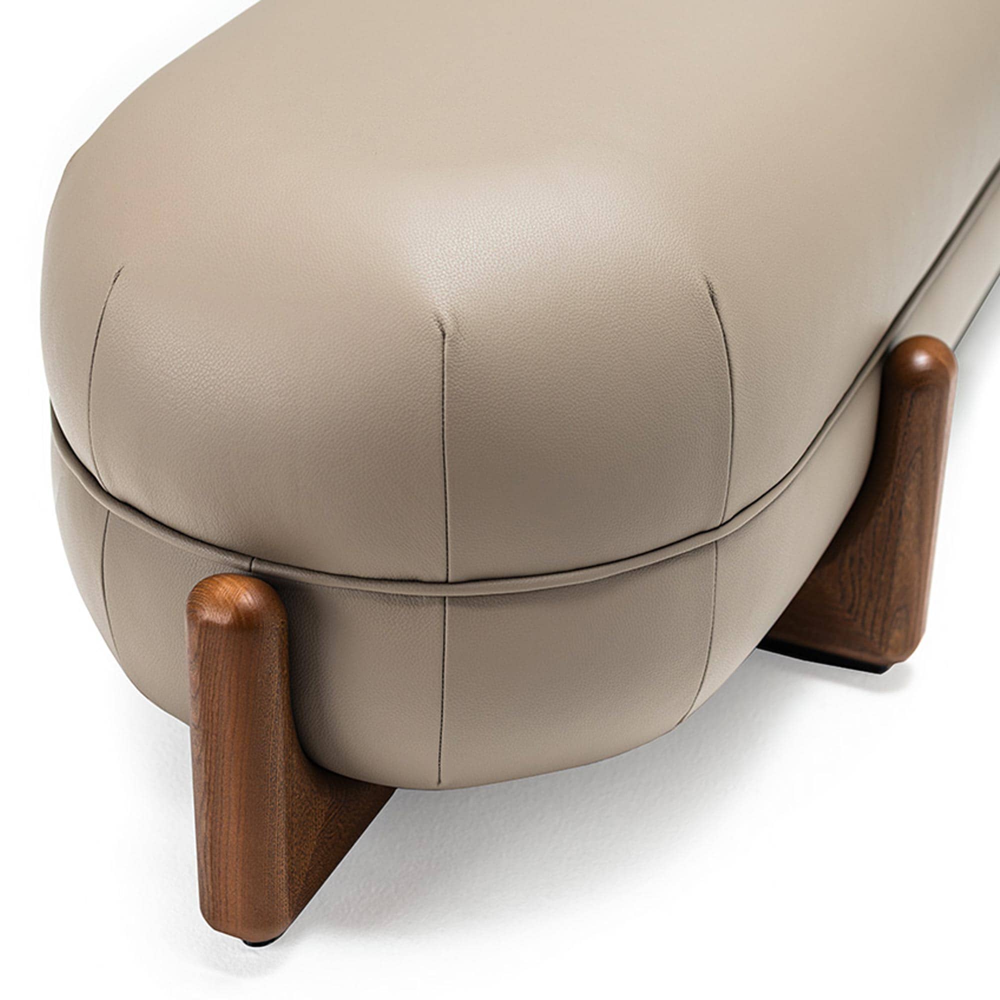 Close-up of a modern beige leather bench with rounded, fluted ends and dark, sculptural wooden legs, against a white background.