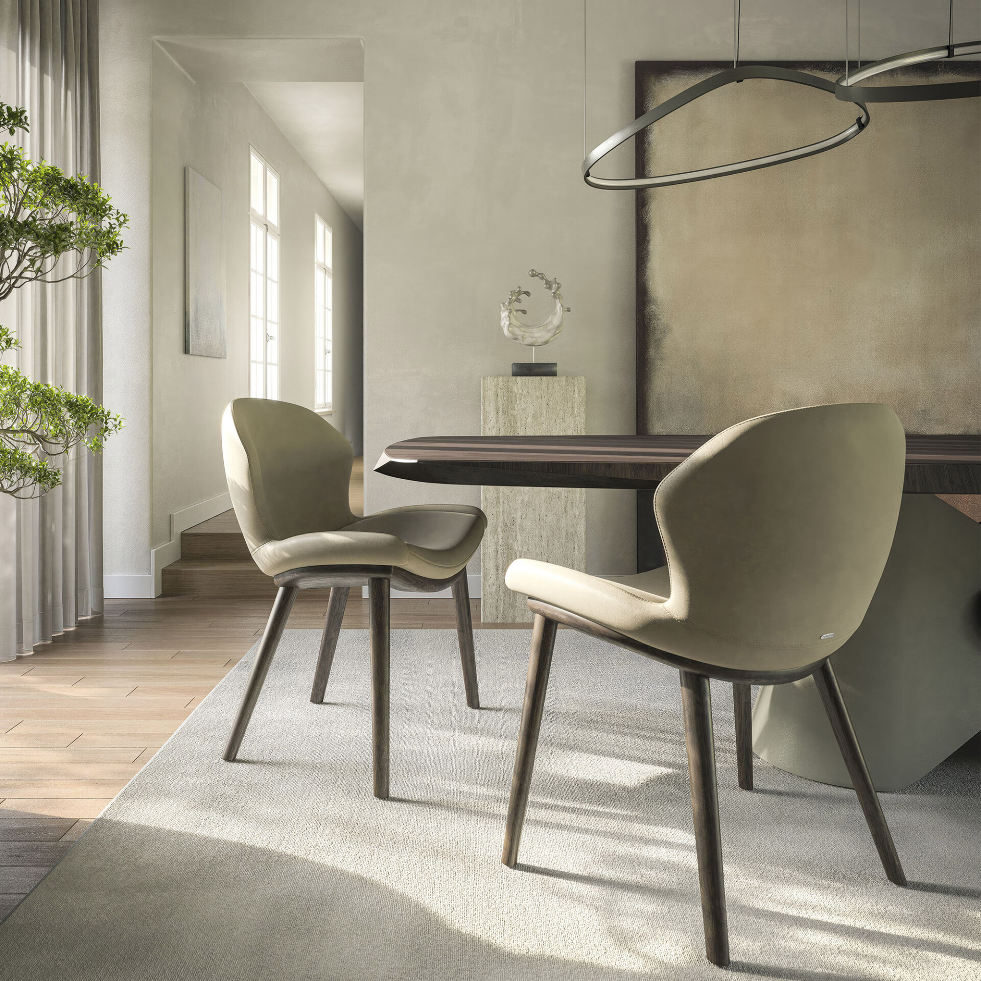 A modern dining room featuring two light beige upholstered chairs, a dark wood dining table, and a minimalist oval pendant light. Natural light streams in, casting shadows on the light-colored rug and textured walls.