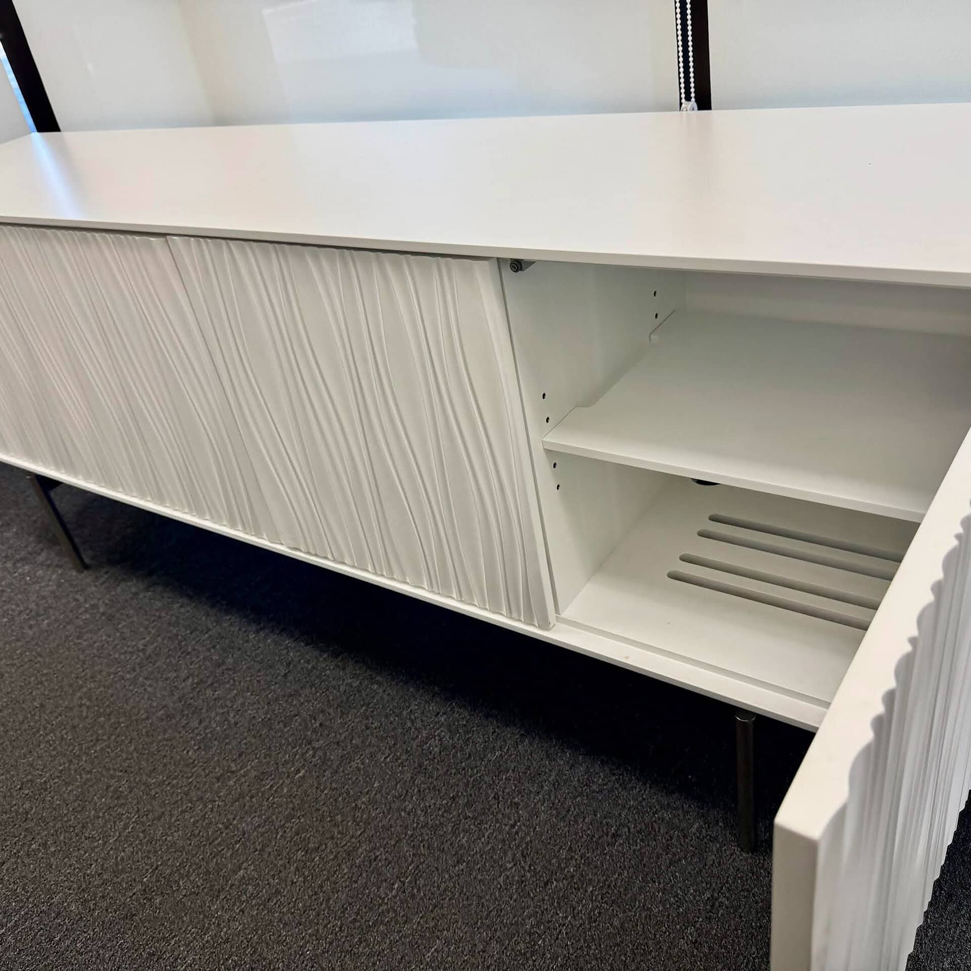 Stylish white entertainment center with textured doors and ample open shelving for TV and media accessories.