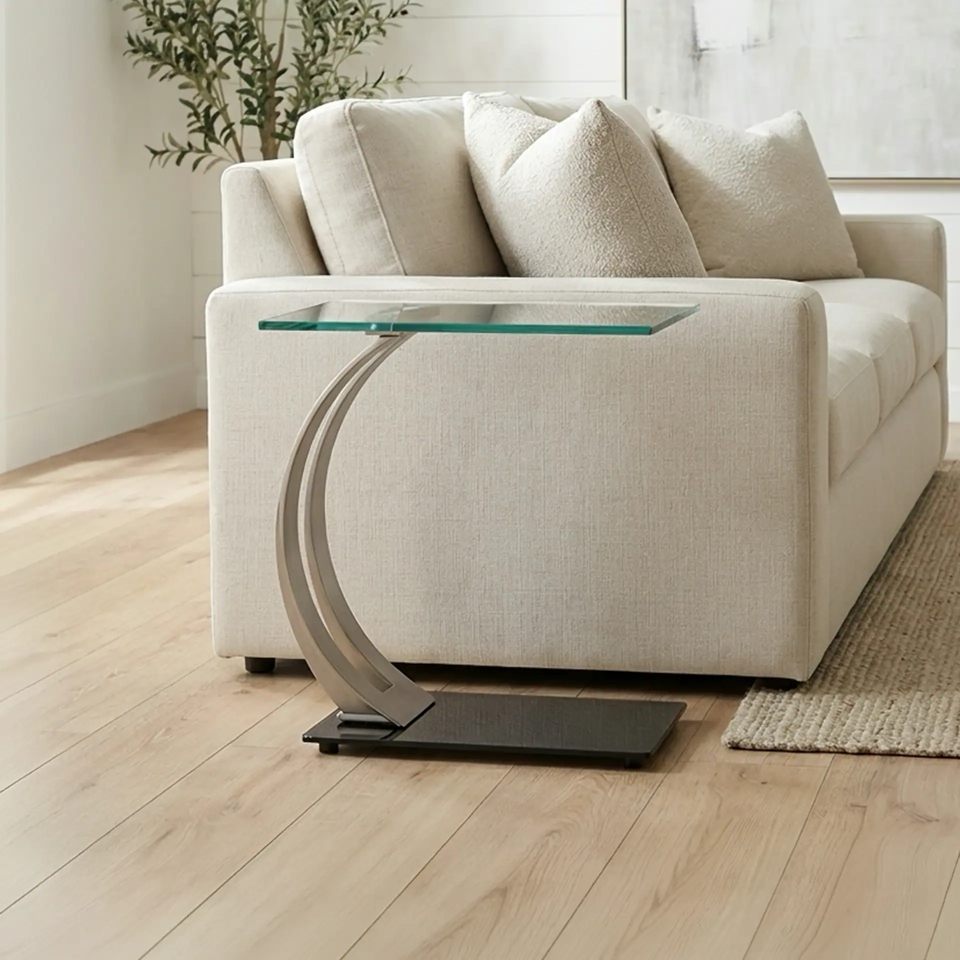 Elegant glass-top sofa side table with unique curved metal base for modern interiors.