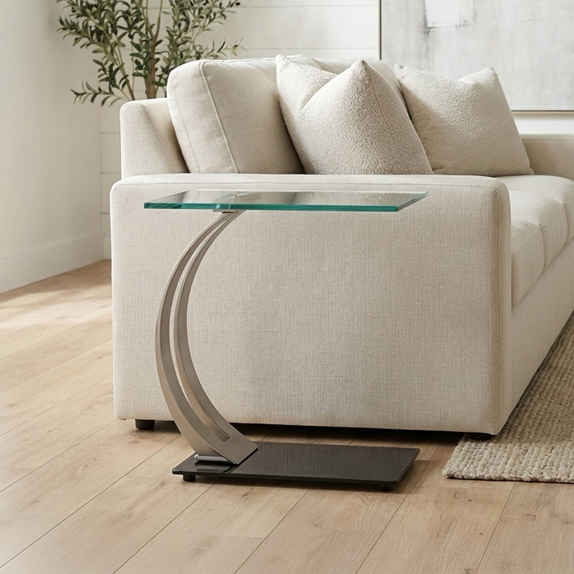 Elegant glass-top sofa side table with unique curved metal base for modern interiors.