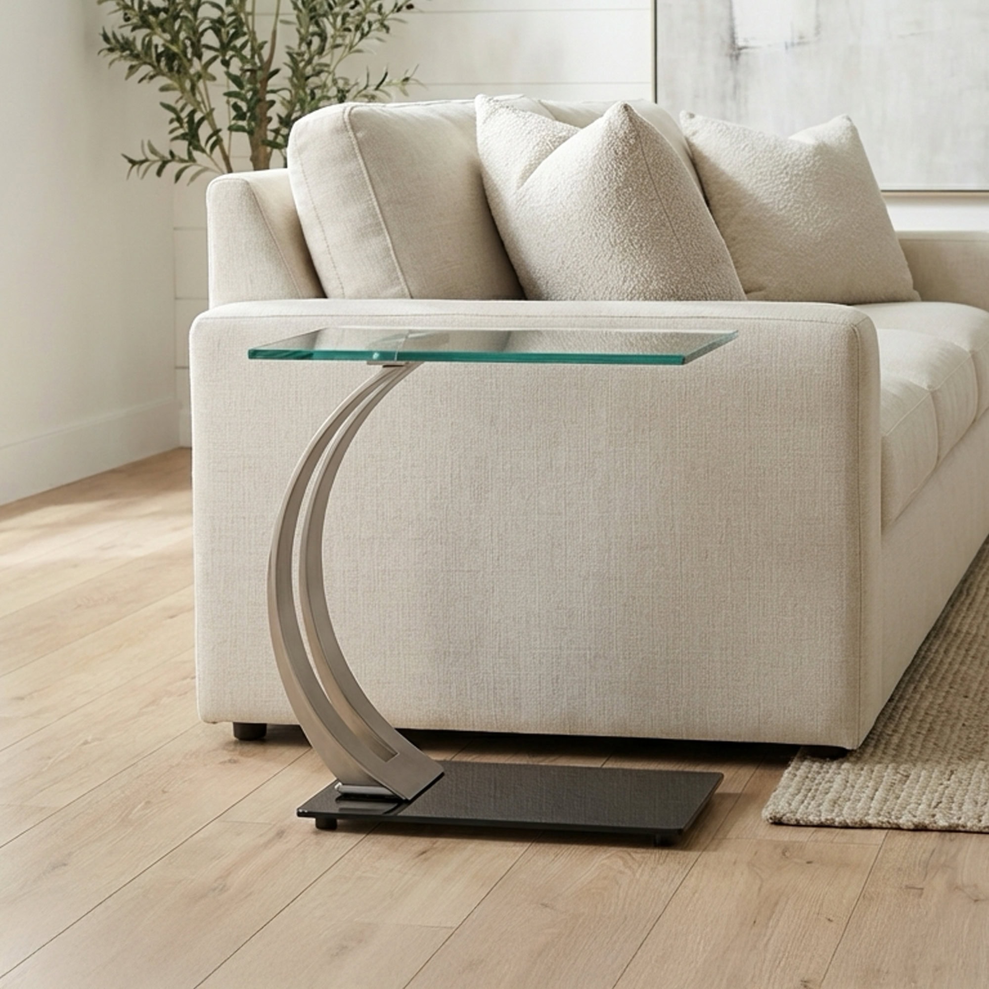 Elegant glass-top sofa side table with unique curved metal base for modern interiors.
